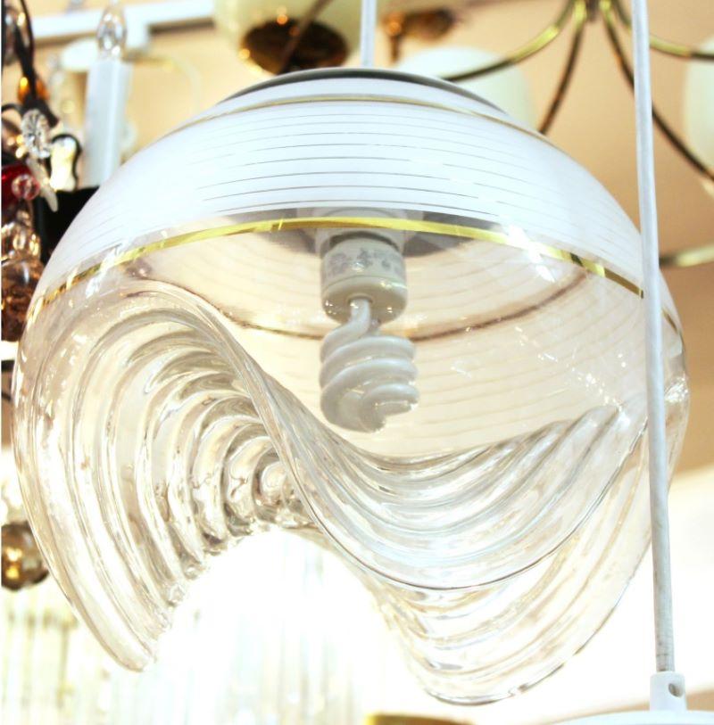 Lustre à pendentif globe en verre sculpté de style moderniste italien,  composé de trois globes sculpturaux en verre semi-opaque et doré avec des sections inférieures ondulées, suspendus à un baldaquin circulaire en métal . 

