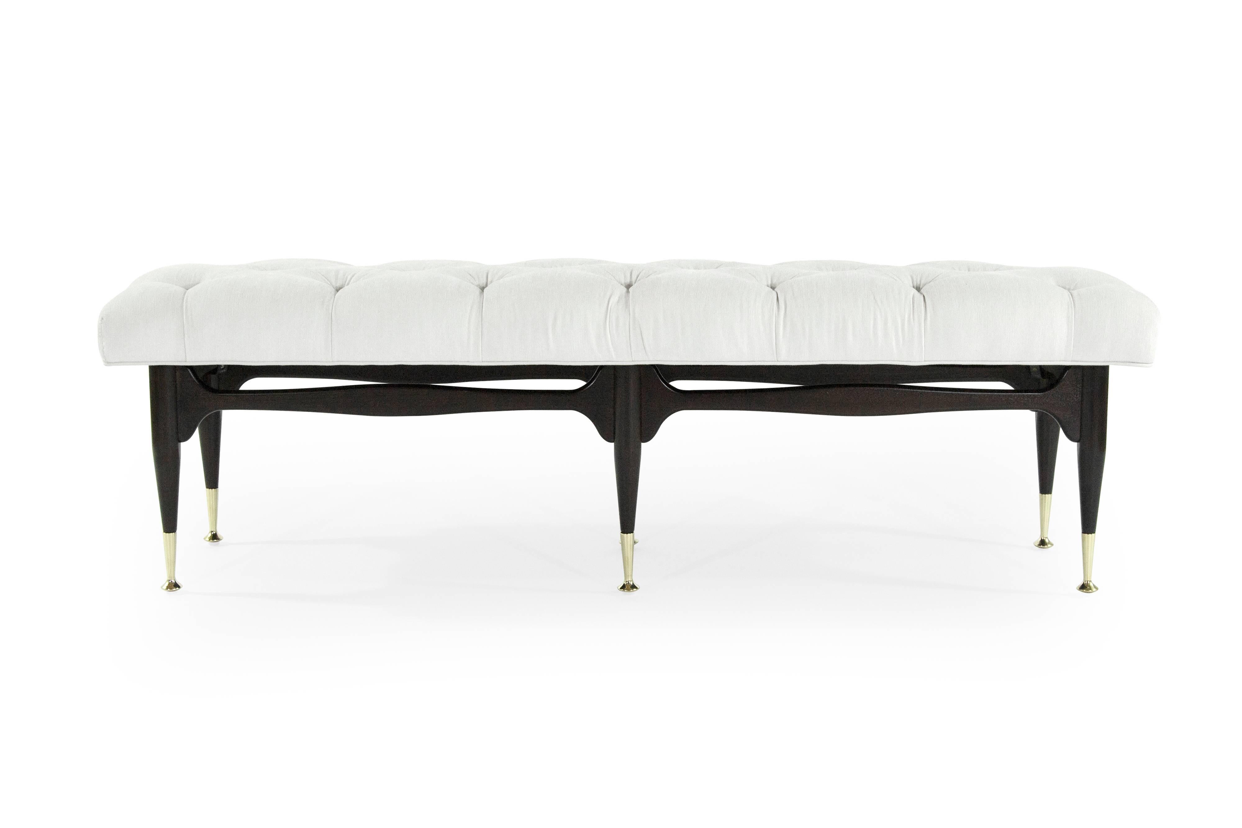 Mid-Century Modern sculpted mahogany bench in the style of Gio Ponti, wood has been fully restored to its original espresso finish. Newly upholstered in off-white cotton linen with tufting detail. Brass sabots newly polished.