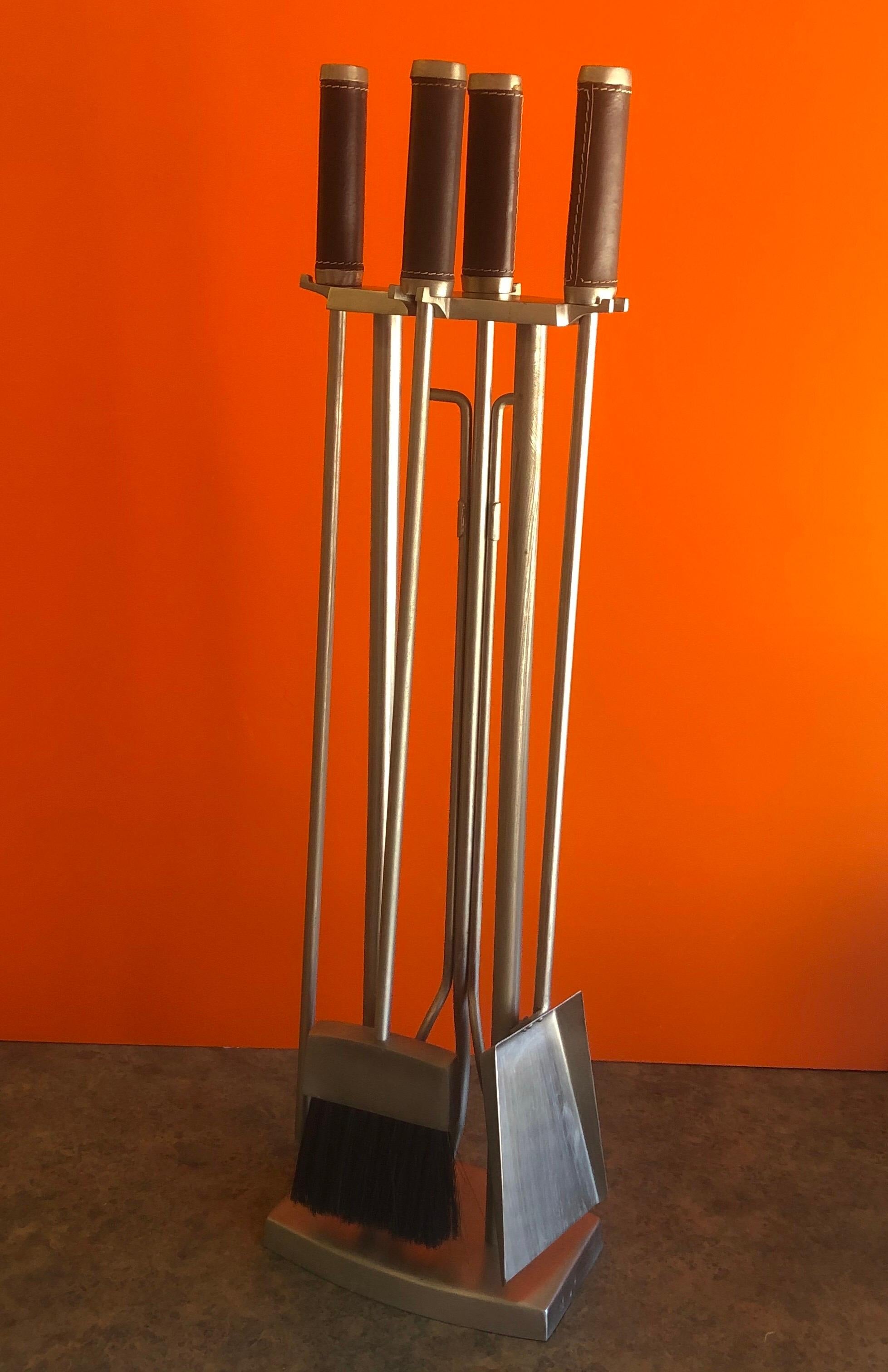 Modernist set of fire place tools in brushed steel with brown leather handles, circa 1970s. There are four tools (shovel, brush, log holder and poker) and a dual column stand in very good vintage condition. The set measures 32