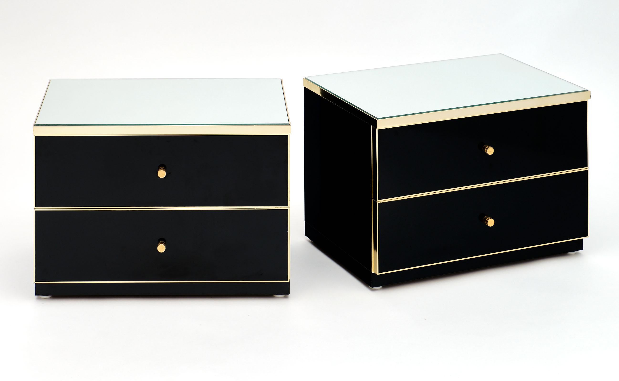 French vintage modernist side tables in the manner of Pierre Cardin. This pair of bedside tables are made of black lacquered wood with gilt aluminum trim. The tops are mirrored. Each features two large drawers. We loved the simplicity and strength