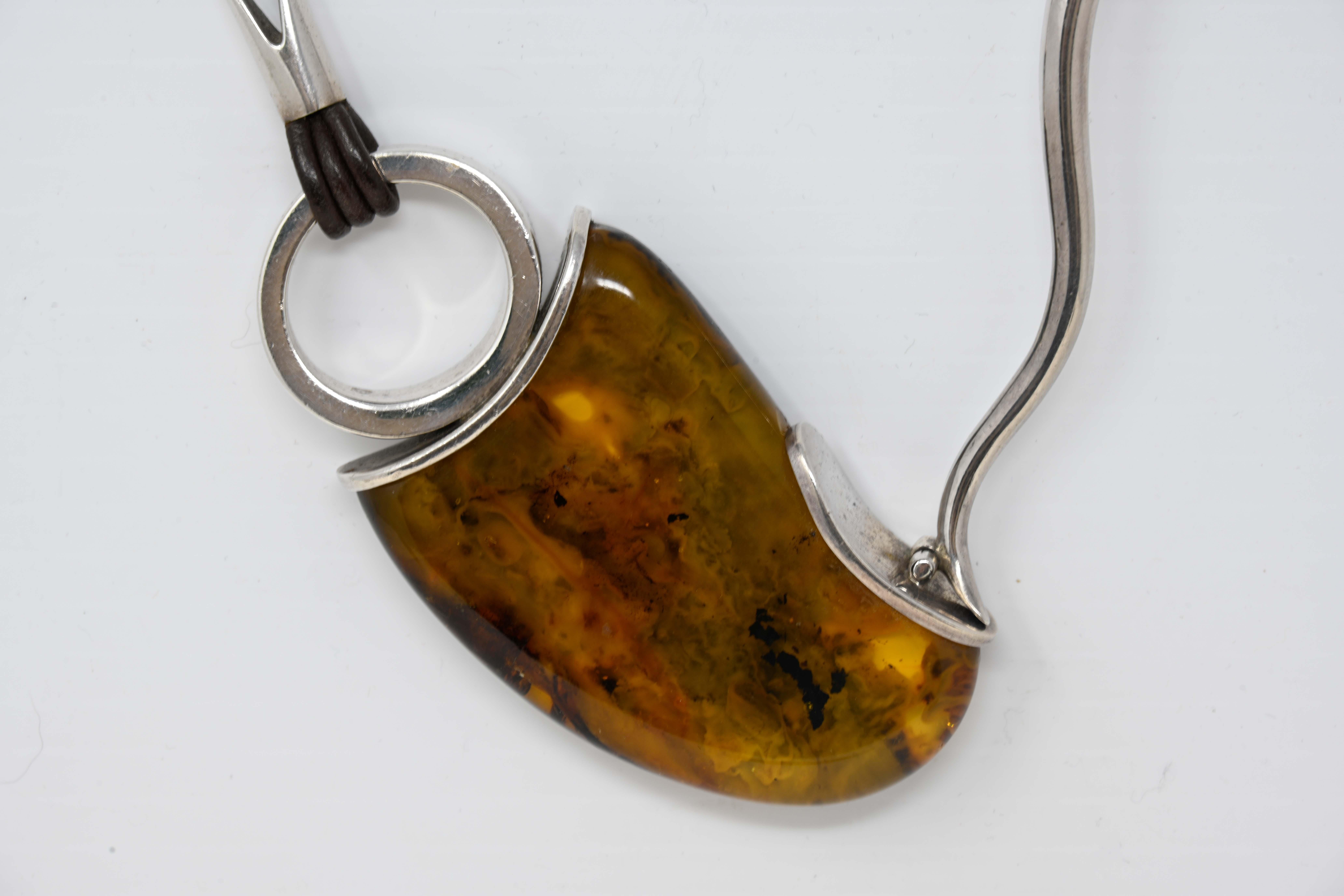 Handmade modernist sterling silver necklace with a large natural Baltic amber. Stamped 925 and includes the maker mark E & M. The amber measures 7cm long x 4.5 cm wide x 1.2 cm thick, The necklace measures 18 inches long, plus the pendant. Preowned,