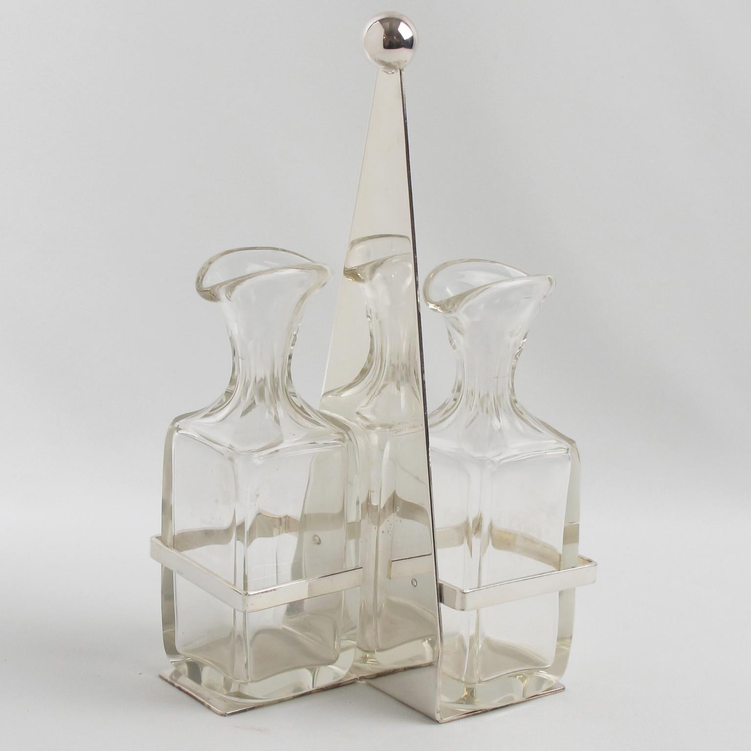 Este precioso accesorio de servicio de mesa modernista Art Decó de los años 30, diseñado por Quist, Alemania, presenta una base geométrica de metal plateado con un asa alta rematada con una bola metálica. Las dos botellas o recipientes de cristal