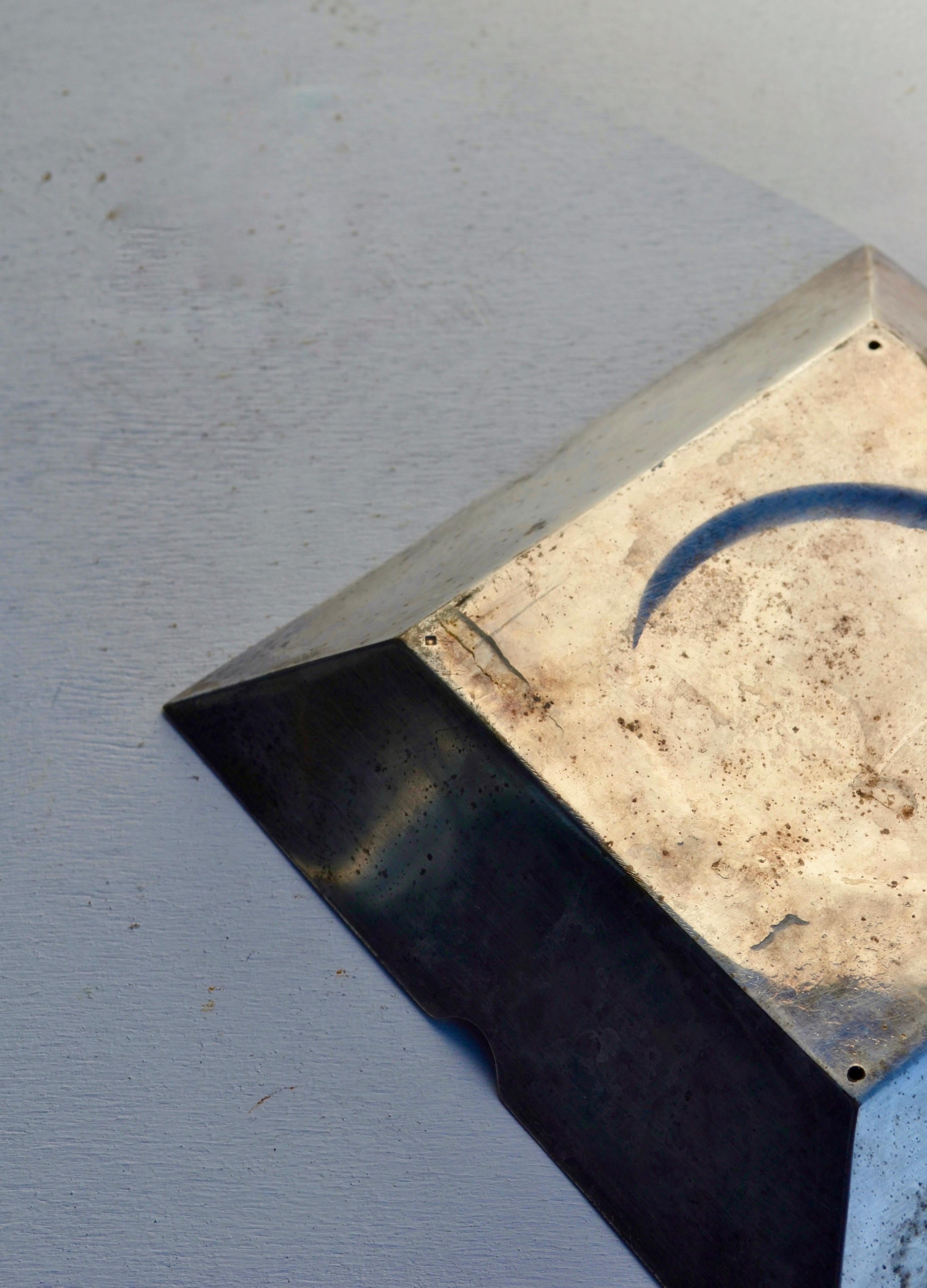 Elegante posacenere modernista in metallo argentato, Francia, circa 1970.
Il pezzo presenta un'audace forma geometrica con una base quadrata e una profonda ciotola circolare, accentuata da quattro tacche su ogni lato. La sua splendida patina