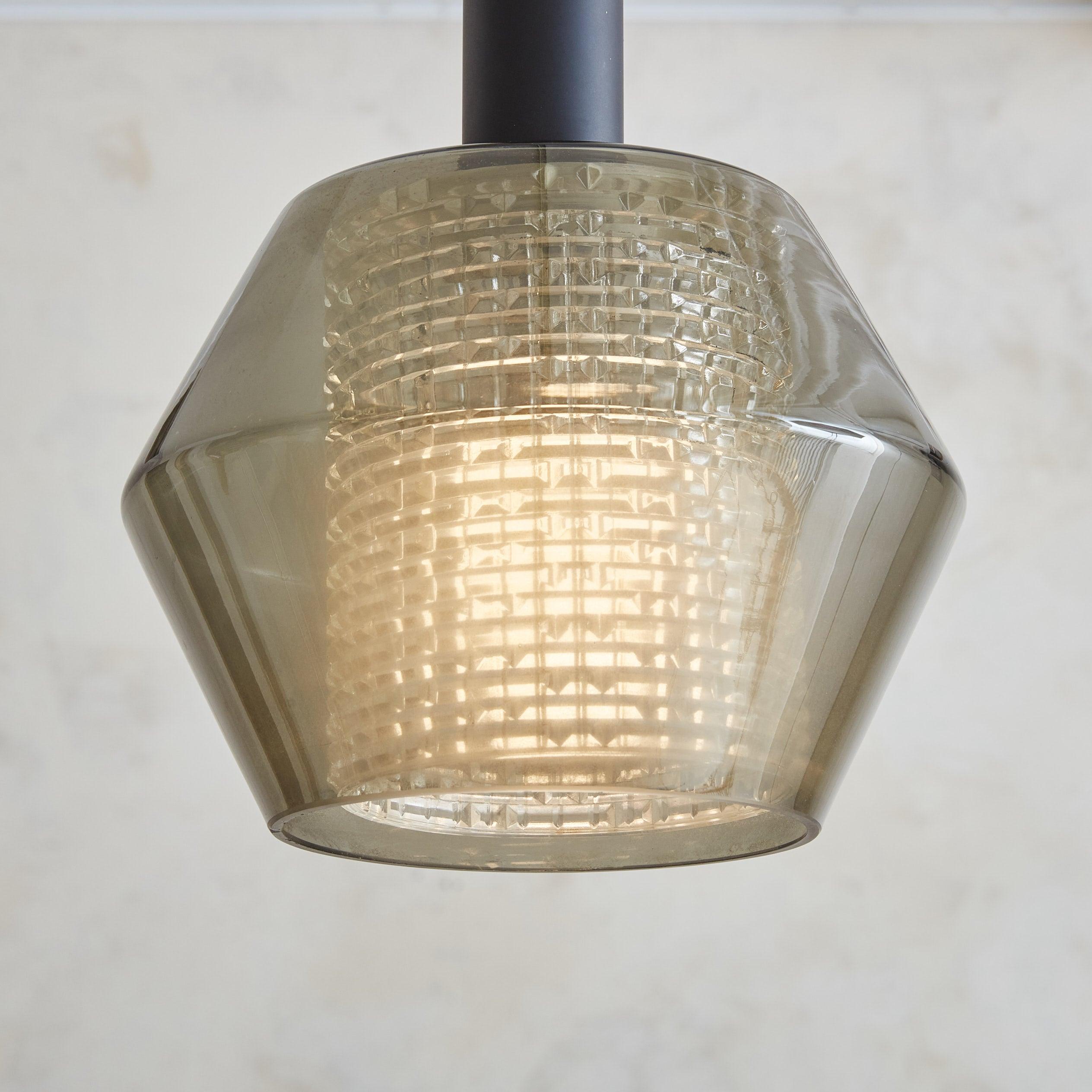 A 1960s pendant light produced by Lightolier in Sweden and distributed in the U.S. This Modernist fixture features a geometric smoked glass outer shade in a gorgeous gray hue, which surrounds a textured glass diffuser. The shade suspends from a