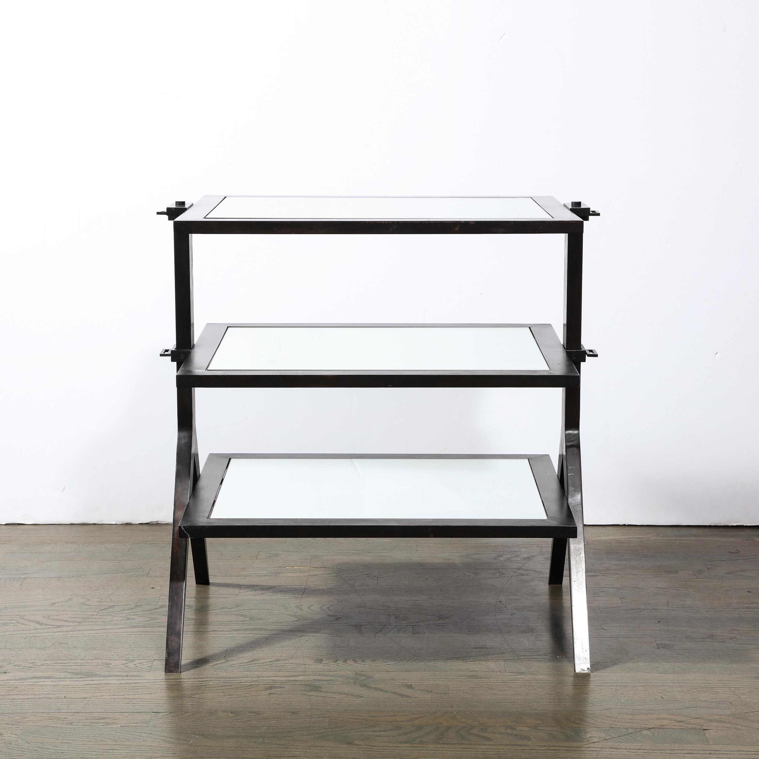 This sophisticated modernist three tier occasional table was realized in the United States circa 1990. It features three rectangular tiers with mirrored centers that adjoin to rectangular side supports that split into compass style tapered feet- all