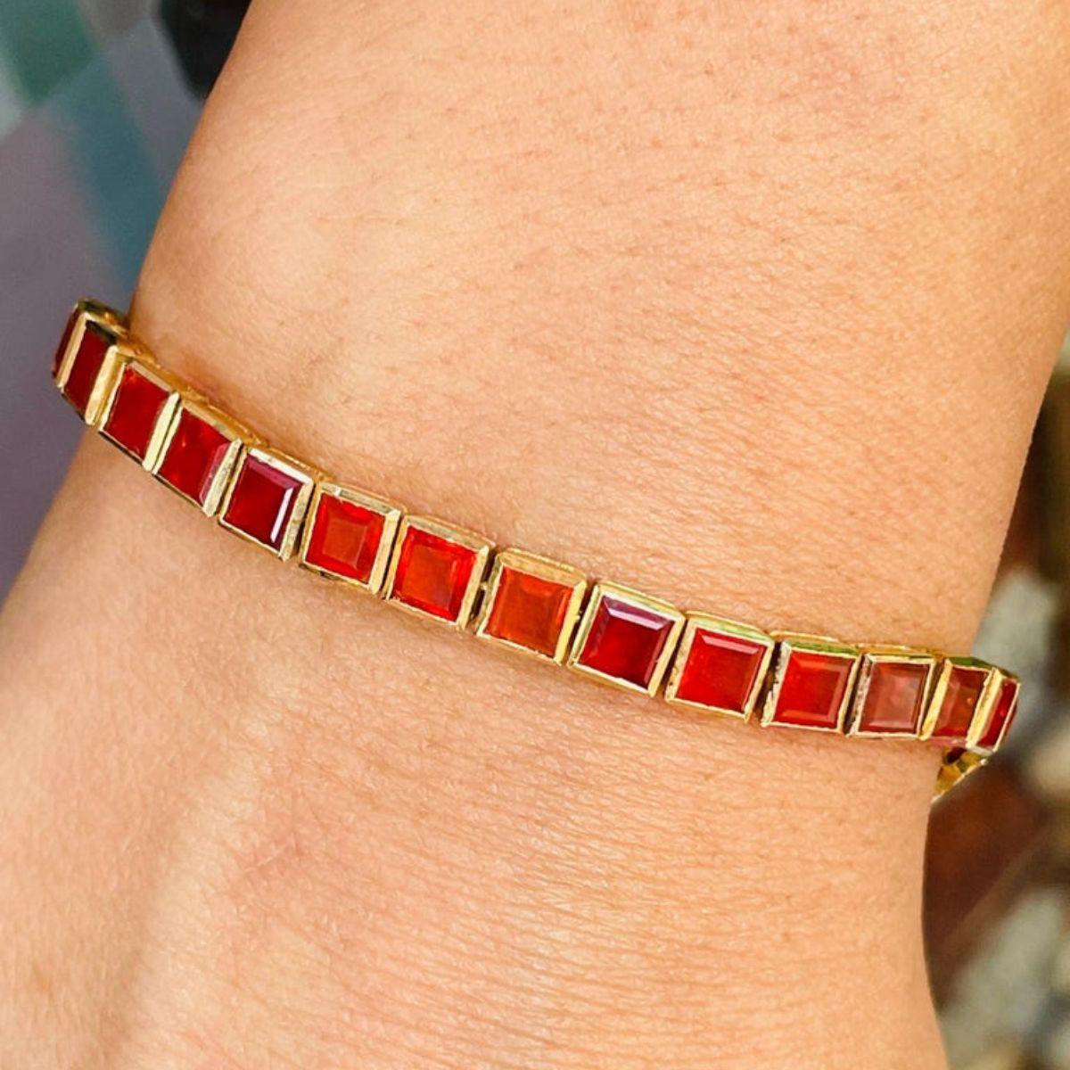 Esta Modernista Pulsera de Tenis de Ópalo Naranja de Corte Cuadrado para Ella en Oro Amarillo de 18 quilates exhibe 35 ópalos naturales de brillo infinito, con un peso de 7,15 quilates. Mide 7 pulgadas de largo. 
El ópalo ayuda a encontrar el amor,