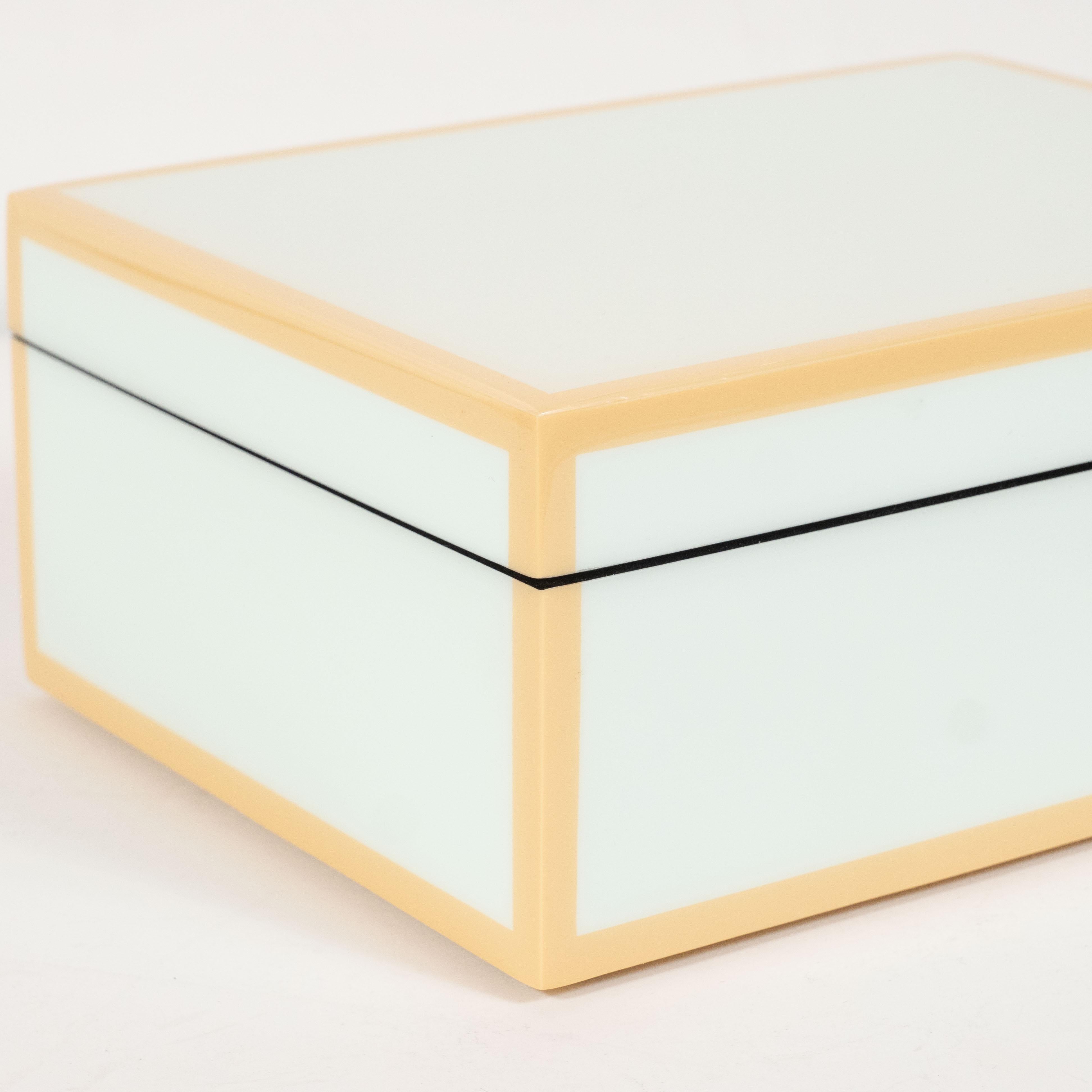This elegant modernist lacquered box offers a square form with a lacquered exterior in a pale celadon hue with tan accents circumscribing each of the exterior edges. The interior of the box has been finished in black felt, testifying to the fact