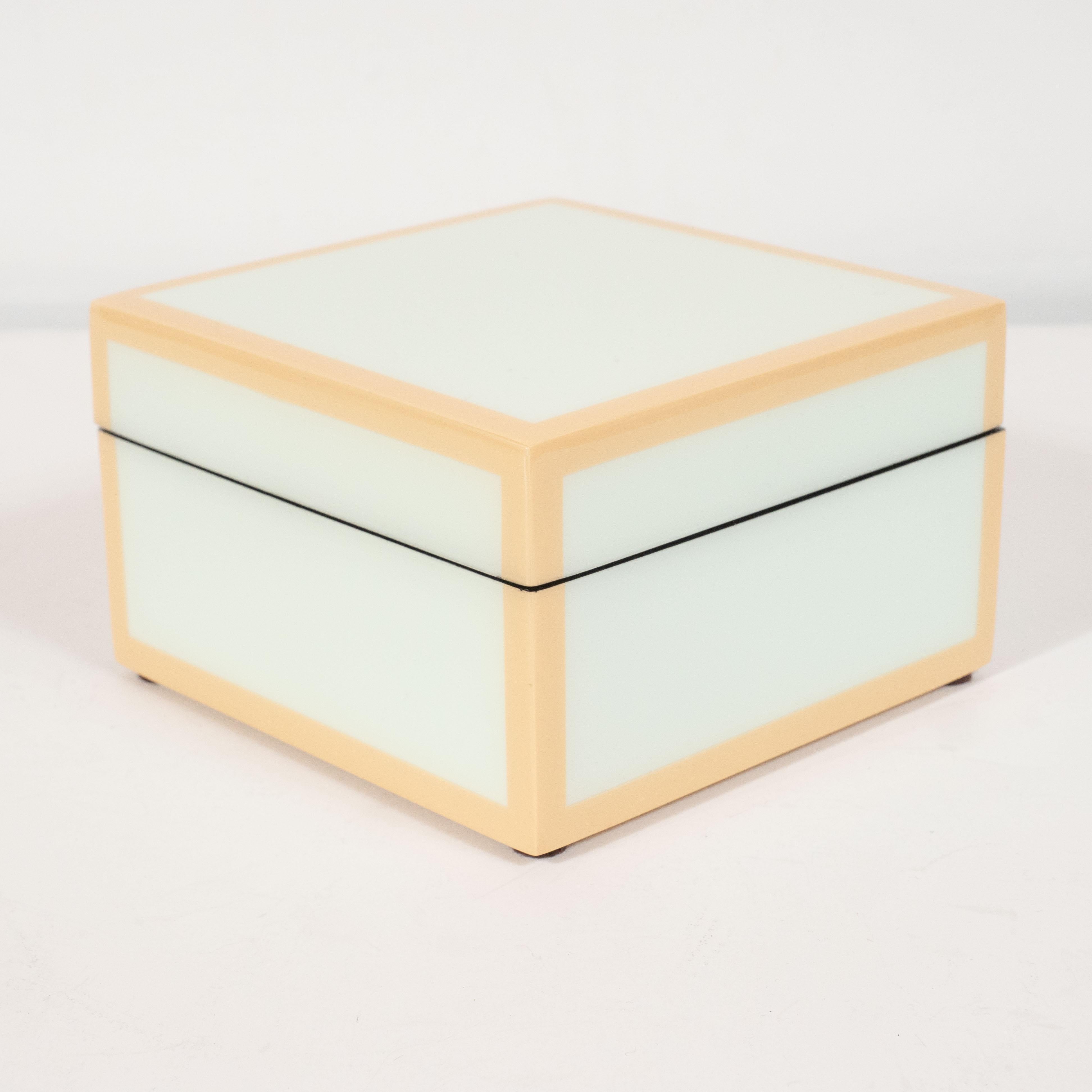 This elegant modernist lacquered box offers a square form with a lacquered exterior in a pale celadon hue with tan accents circumscribing each of the exterior edges. The interior of the box has been finished in black felt, testifying to the fact
