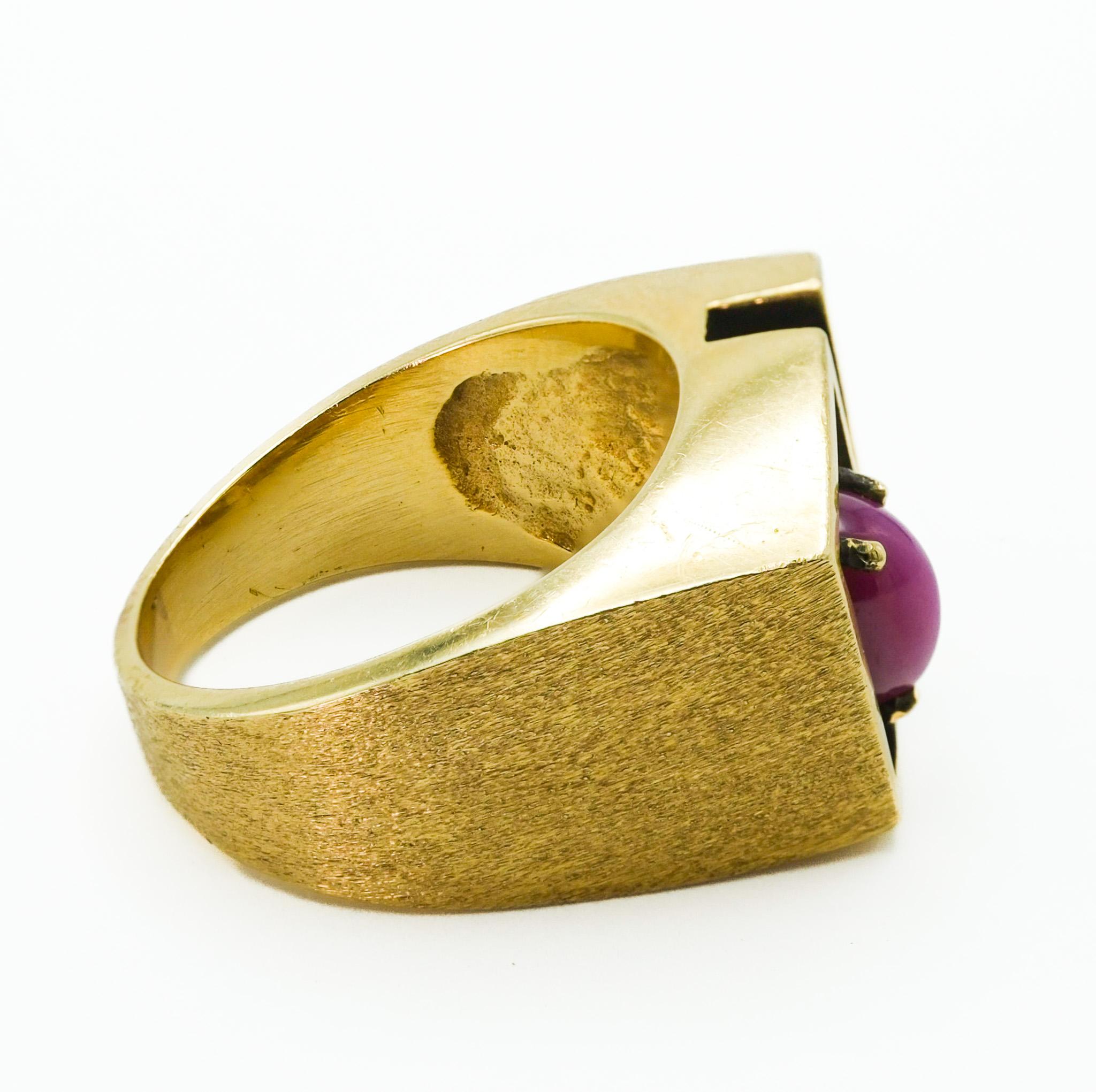 This 14k yellow gold ring presents a unique and distinct structural design. Its form is noticeably large and boxy, departing from conventional ring shapes. At the center of the piece lies a teardrop star ruby, weighing 1 carat, displaying a