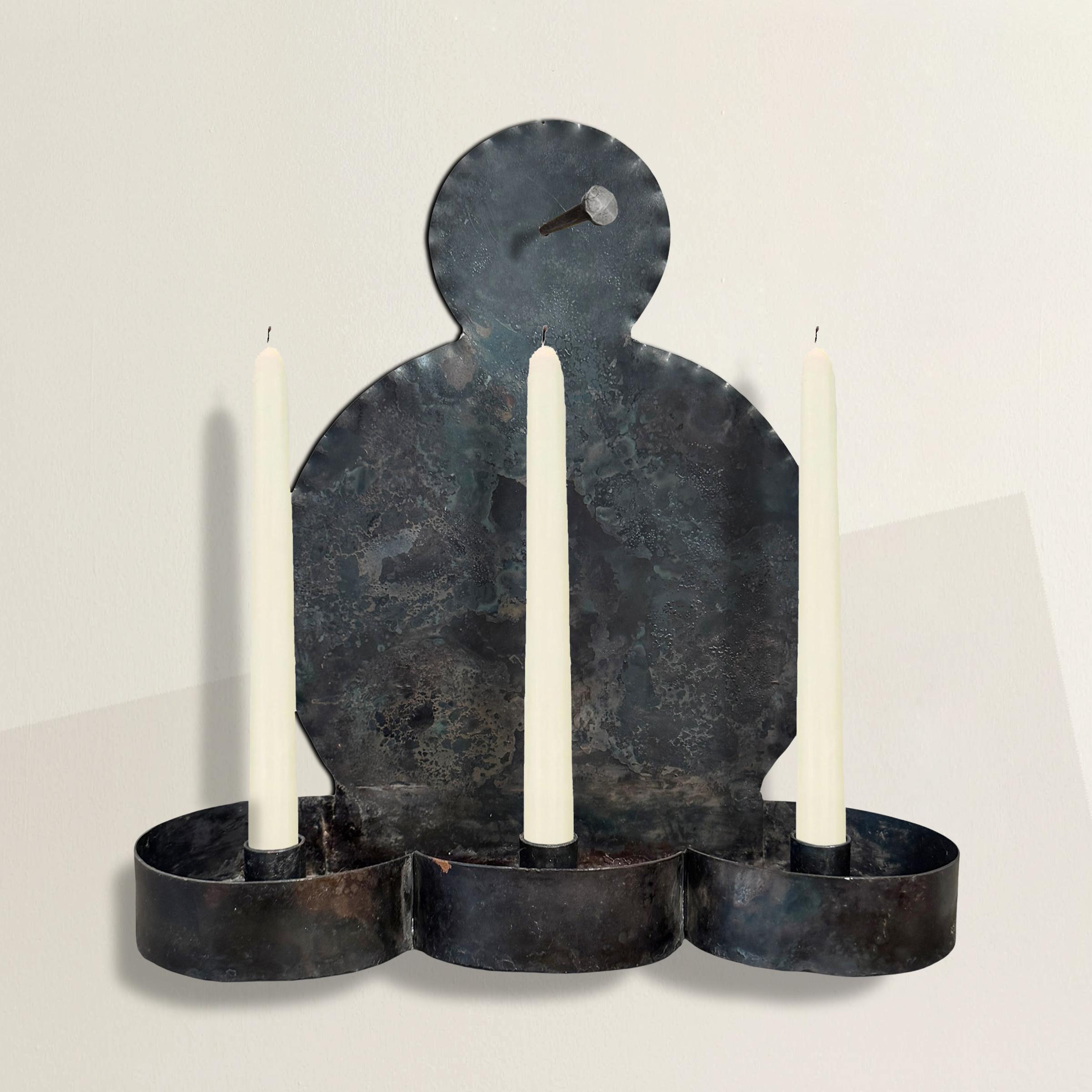 With its bold geometry and elemental presence, this 21st-century steel sconce reads as both strikingly modern and unmistakably rooted in early American tradition. Three deep candle cups anchor the base—scalloped like a Shaker bonnet rack—while the