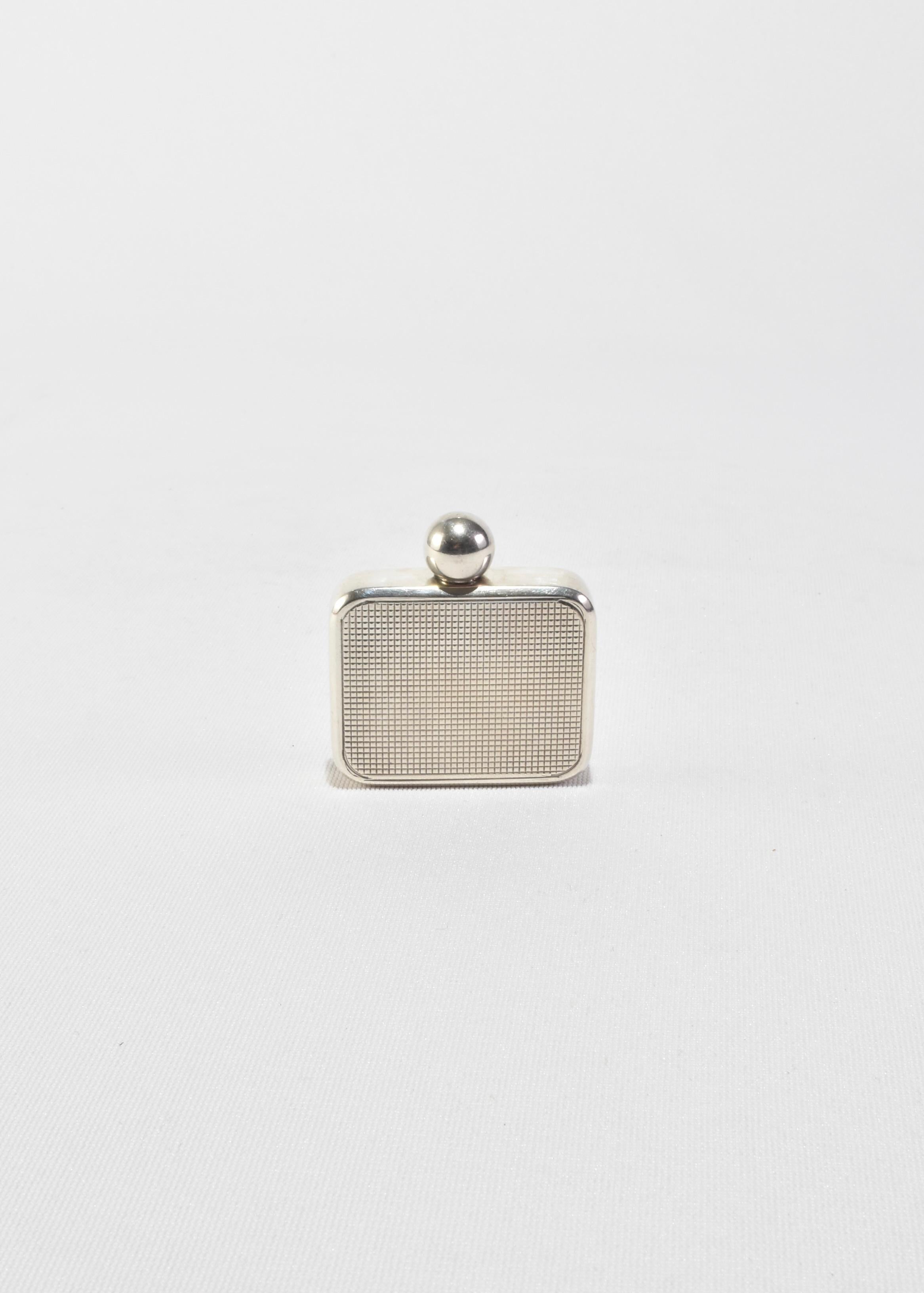 Ein kompakter Parfümflakon aus Sterlingsilber, gestempelt 925, mit einer fein strukturierten Vorderseite und einer sanft abgerundeten quadratischen Form. Mit einem glatten, kugelförmigen Stopfen versehen, ist dieses Stück sowohl funktionell als auch