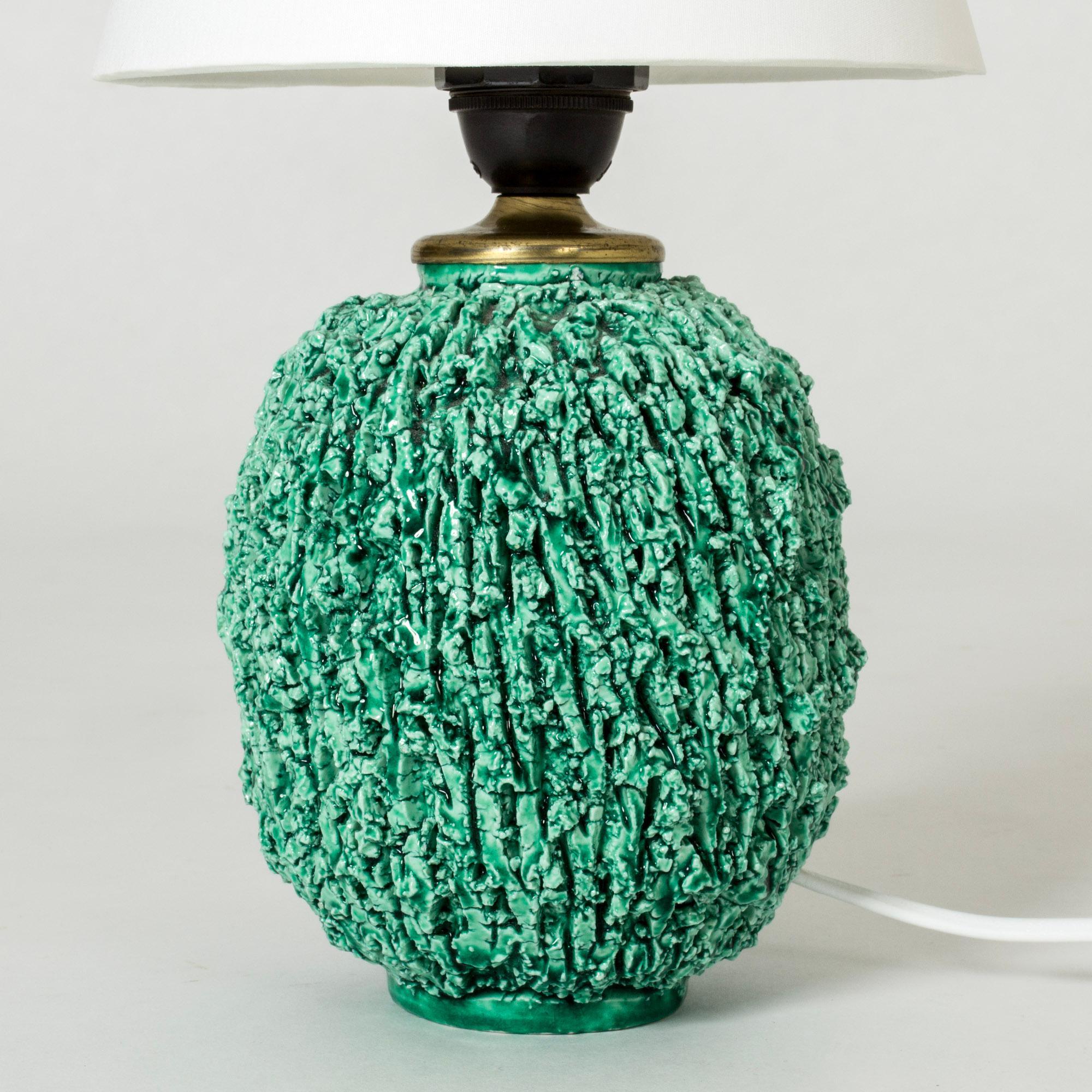 Striking table lamp by Gunnar Nylund, made in chamotte stoneware in Nylund’s “Hedgehog” model. The clean form contrasts with the craggy surface. Vibrant green glaze.

The model was introduced around 1937 and became a great success. It was made with