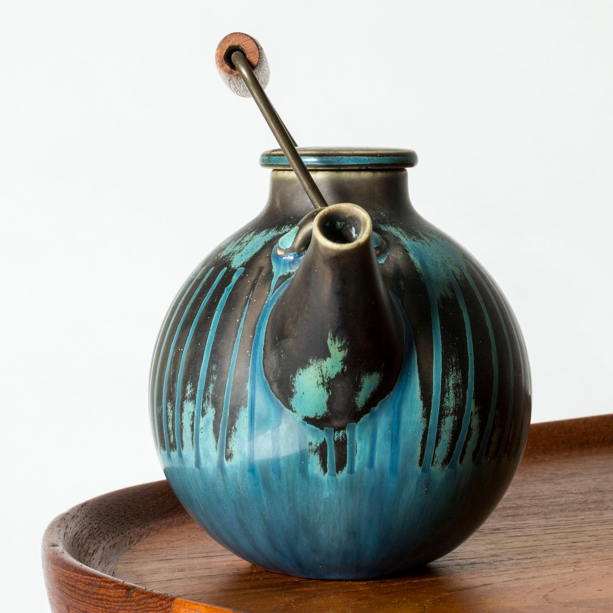 Wunderschöne kleine Teekanne von Stig Lindberg, rund in der Form mit einer schönen ozeanblauen Glasur mit dunkleren Streifen. Hergestellt aus Steingut, mit einem Griff aus Teakholz und Metall.

Er fasst ca. 3 dl, ist also ein Ein-Personen-Topf.
