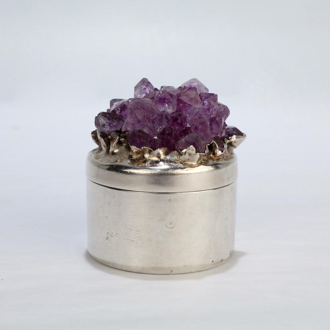 A very good modernist English sterling silver and amethyst covered dresser box.

The lid is set with amethyst gemstones in the manner of Stuart Devlin.

The base is marked for London, sterling silver, 1970, and with a maker's mark SL.

Diameter: ca.