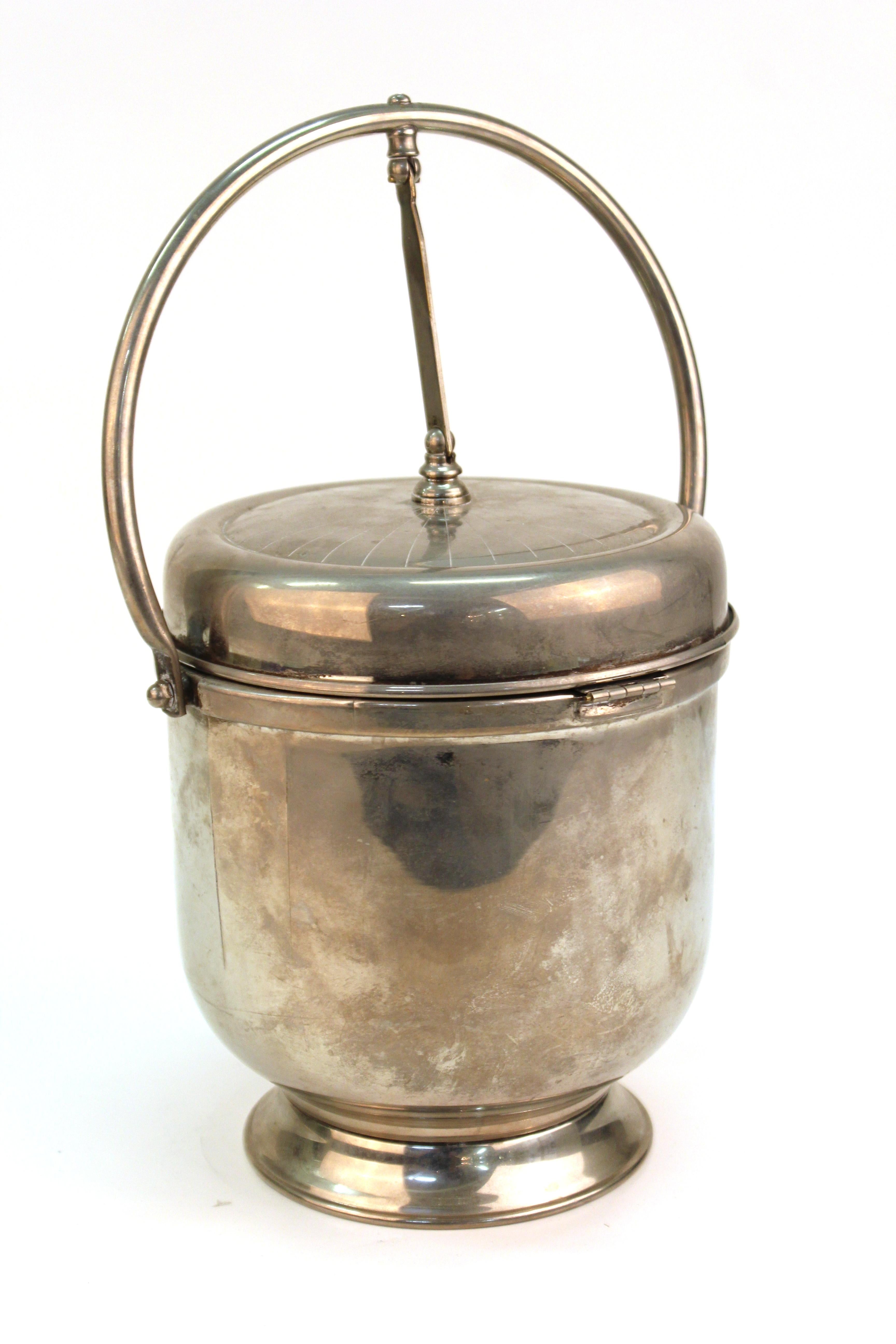 Modernist style ice bucket in chrome with a swinging lid that opens the ice container on one side, and the bar accessories compartment within the lid on the other side. In vintage condition with cracks on both sides of the handles.