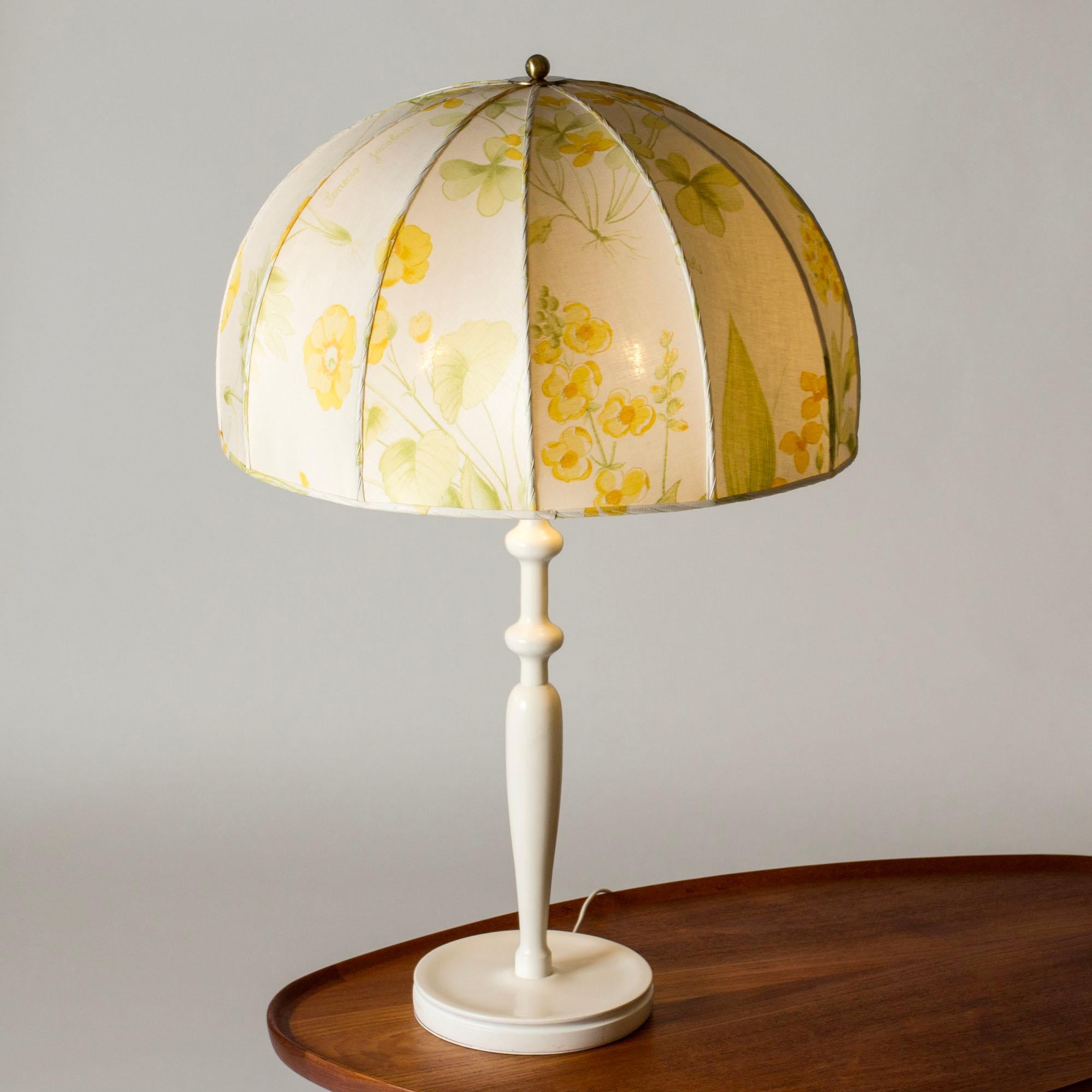 Beautiful table lamp by Josef Frank, model #2563. White lacquered, sculpted wooden base, voluminous shade with textile fabric. Pattern of yellow wildflowers.