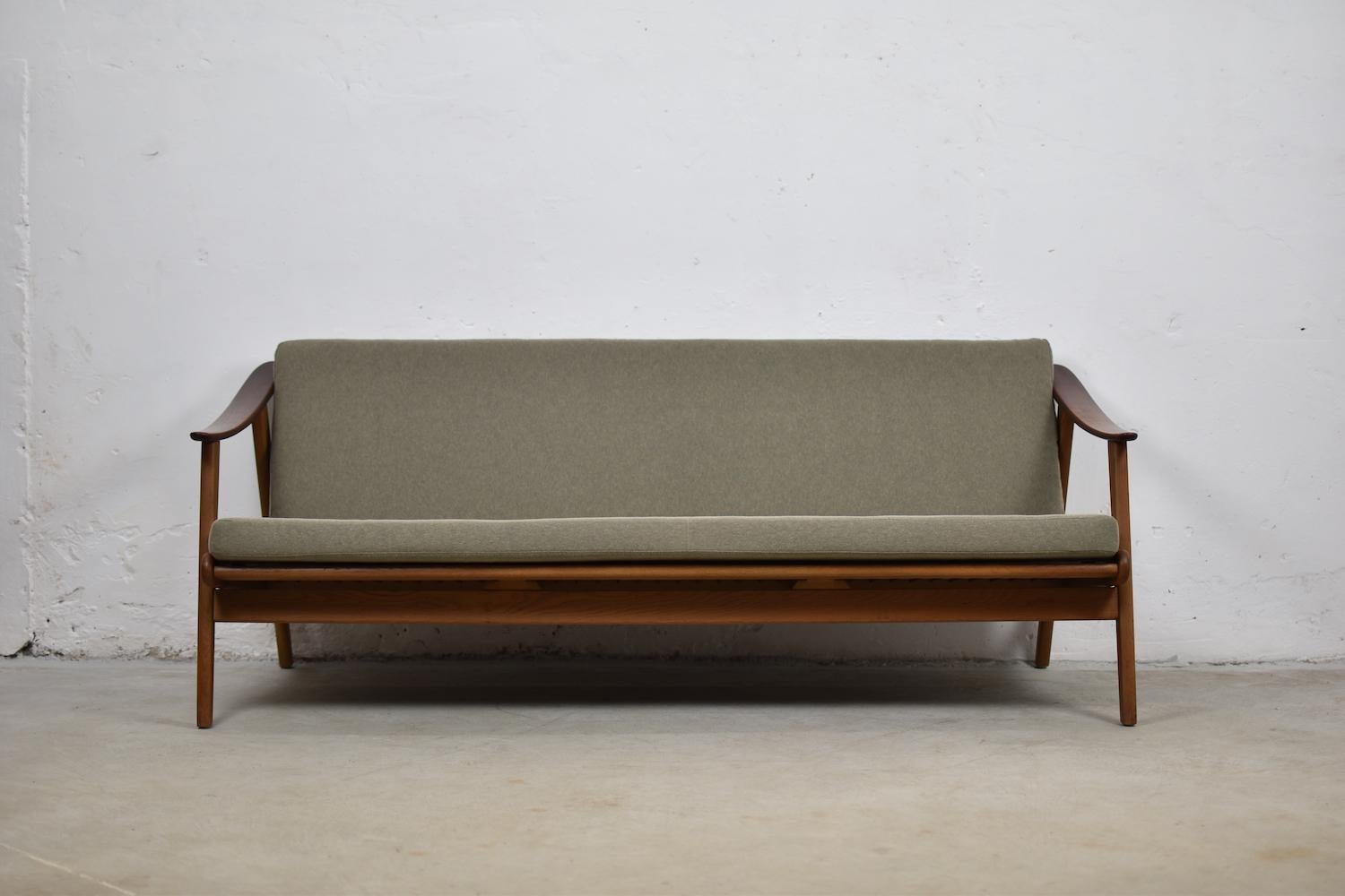 Lovely modernist three-seat from Denmark, 1960s. This sofa is made out of oak and has arm rests made out of teak. Freshly re-upholstered in a grey-green fabric. Clean lines, nice open back. Matching pair of easy chairs is also available.