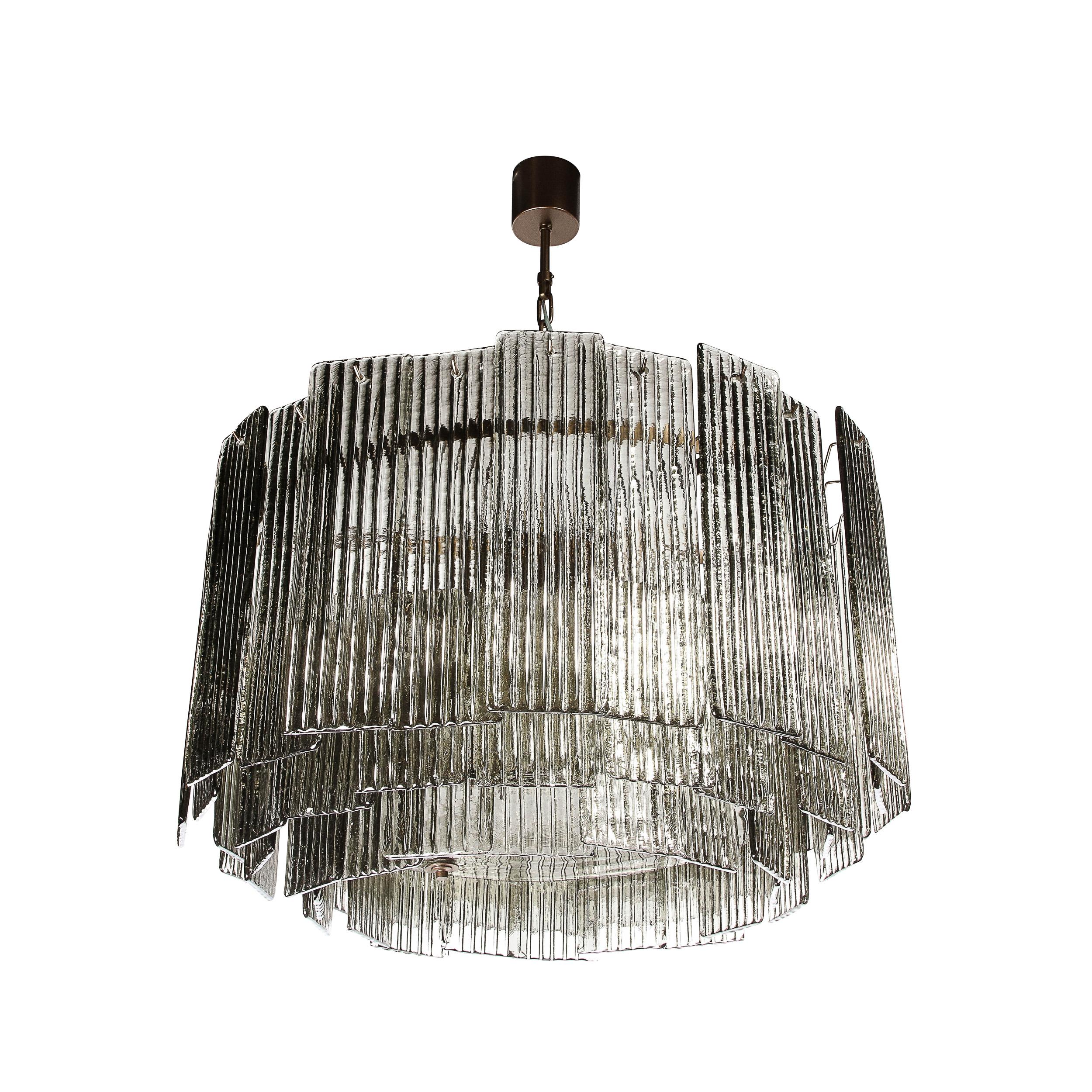 This bold and substantial Modernist Three Tiered Hand-Blown Murano Smoked Topaz Reeded Glass Chandelier originates from Italy during the 21st Century. Featuring large rectangular panels of beautiful reeded glass elements surrounding the piece in