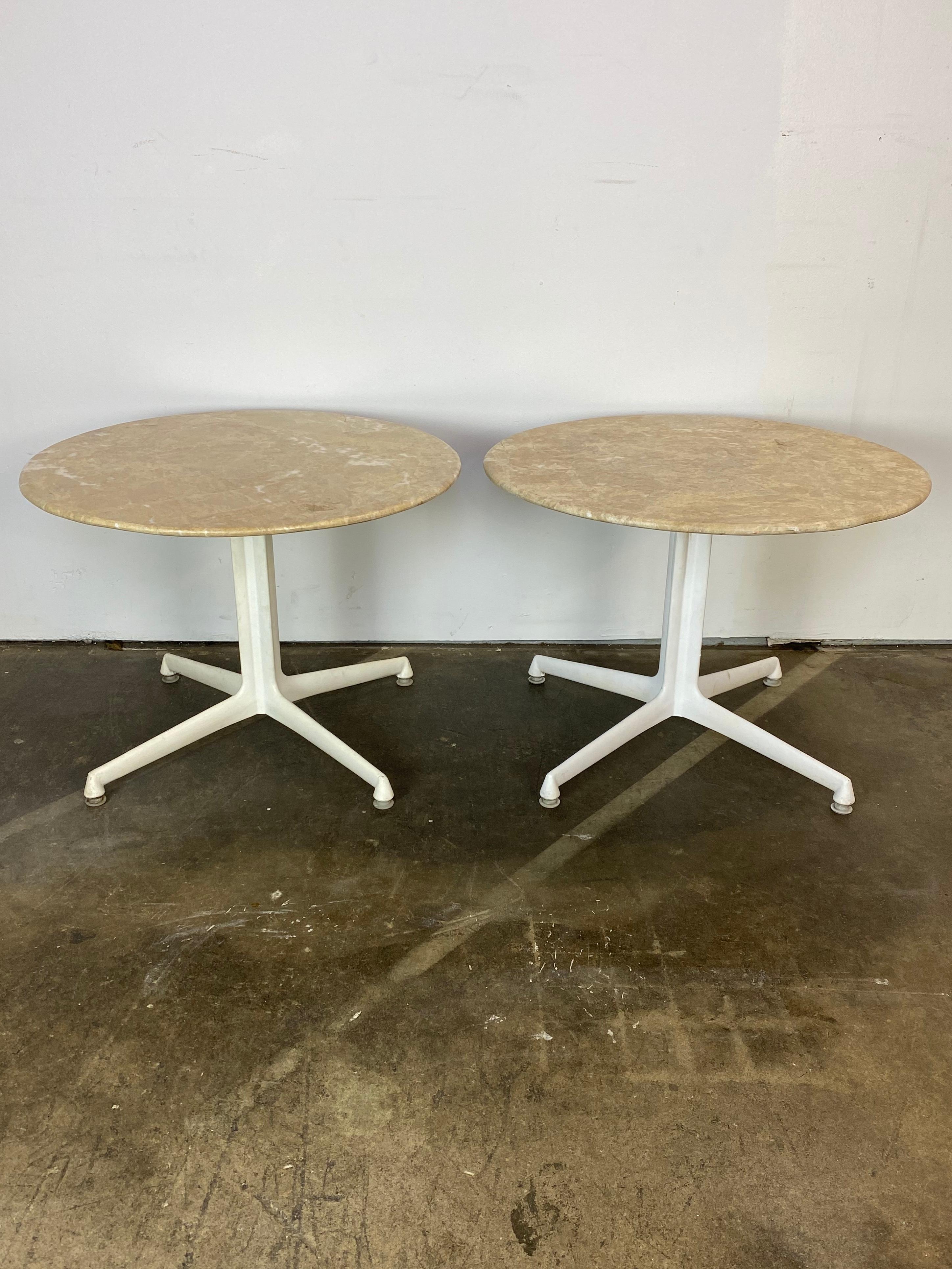 Gorgeous pair or travertine marble side tables. Circular heavy tops rest upon white metal bases in the style of the Eames La Fonda base. Sturdy and firm, these tables are elegant to use at the ends of a sofa, yet large enough to use as bedside