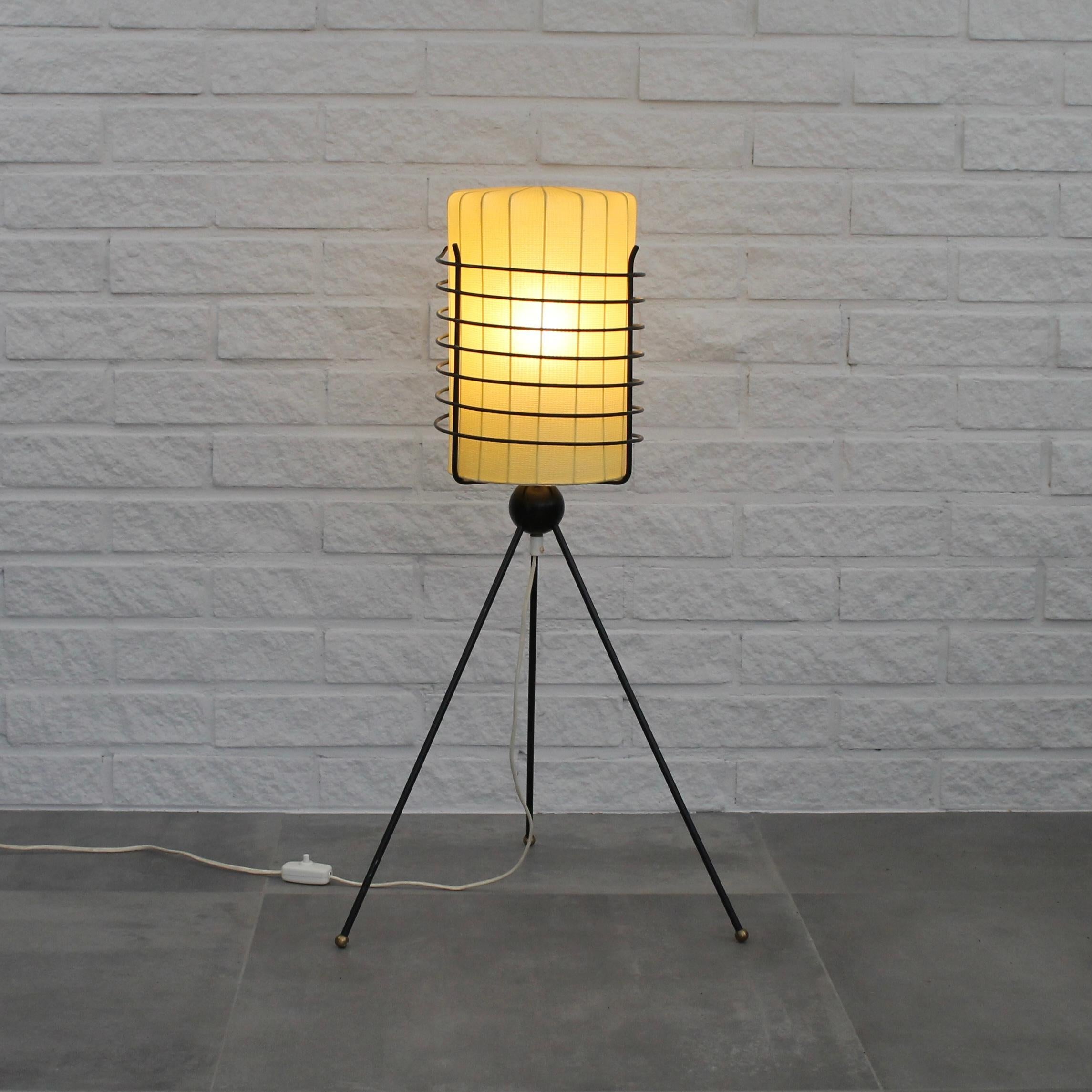 Rare mid-century Swedish floor lamp produced by Trema Industri, c. 1958. The lamp features a metal tripod base with a black metal cage that cradles a cylindrical lampshade enveloped in plastic-coated Texopla textile. Its feet are adorned with small