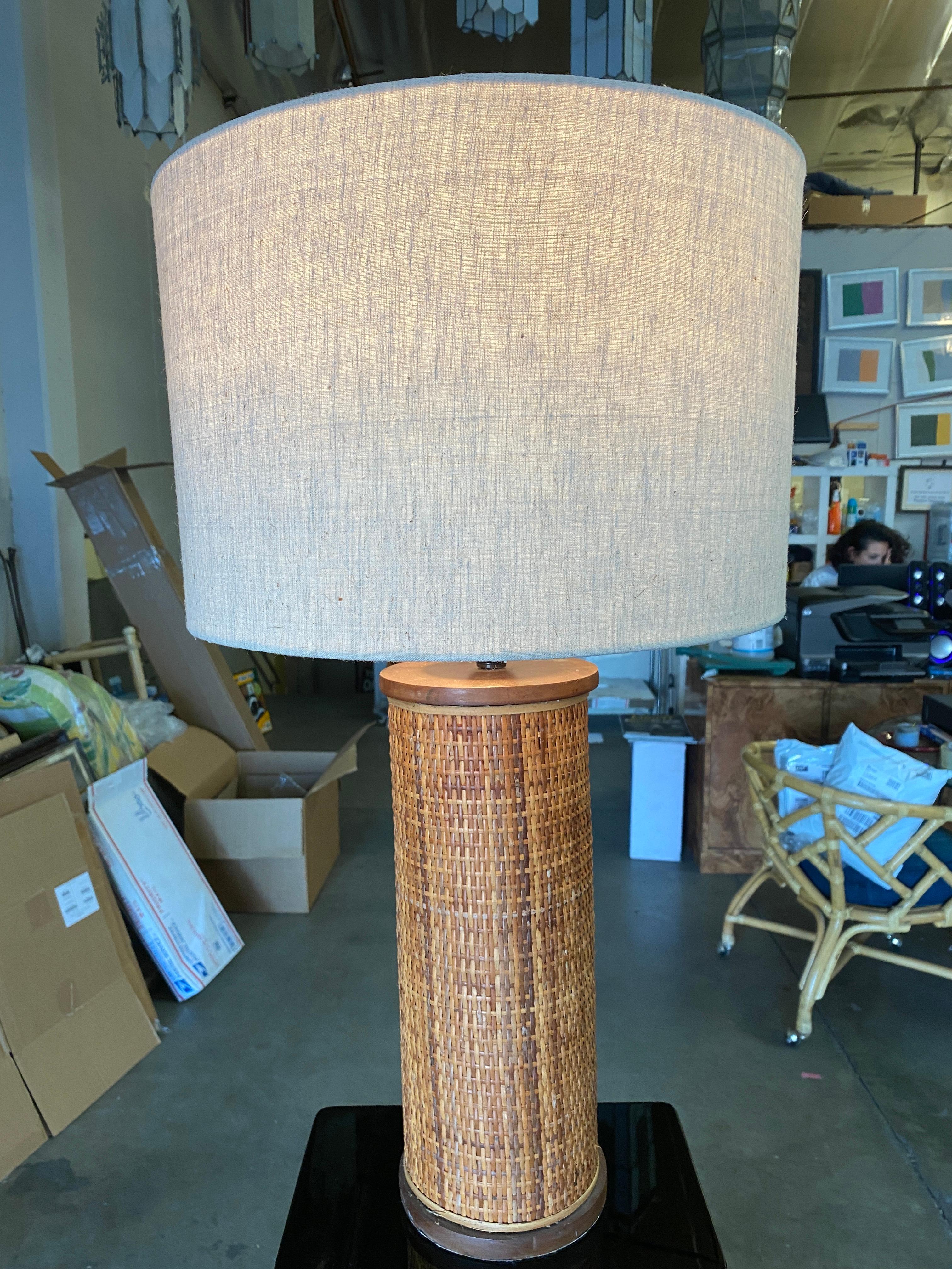 Modernist Circa 1980 lamp featuring a Dark stained mahogany base and top plate wrapped in decorative strung woven wicker grass-mat side. The lamp comes with its original Fabric Shade.

Lamp: 16