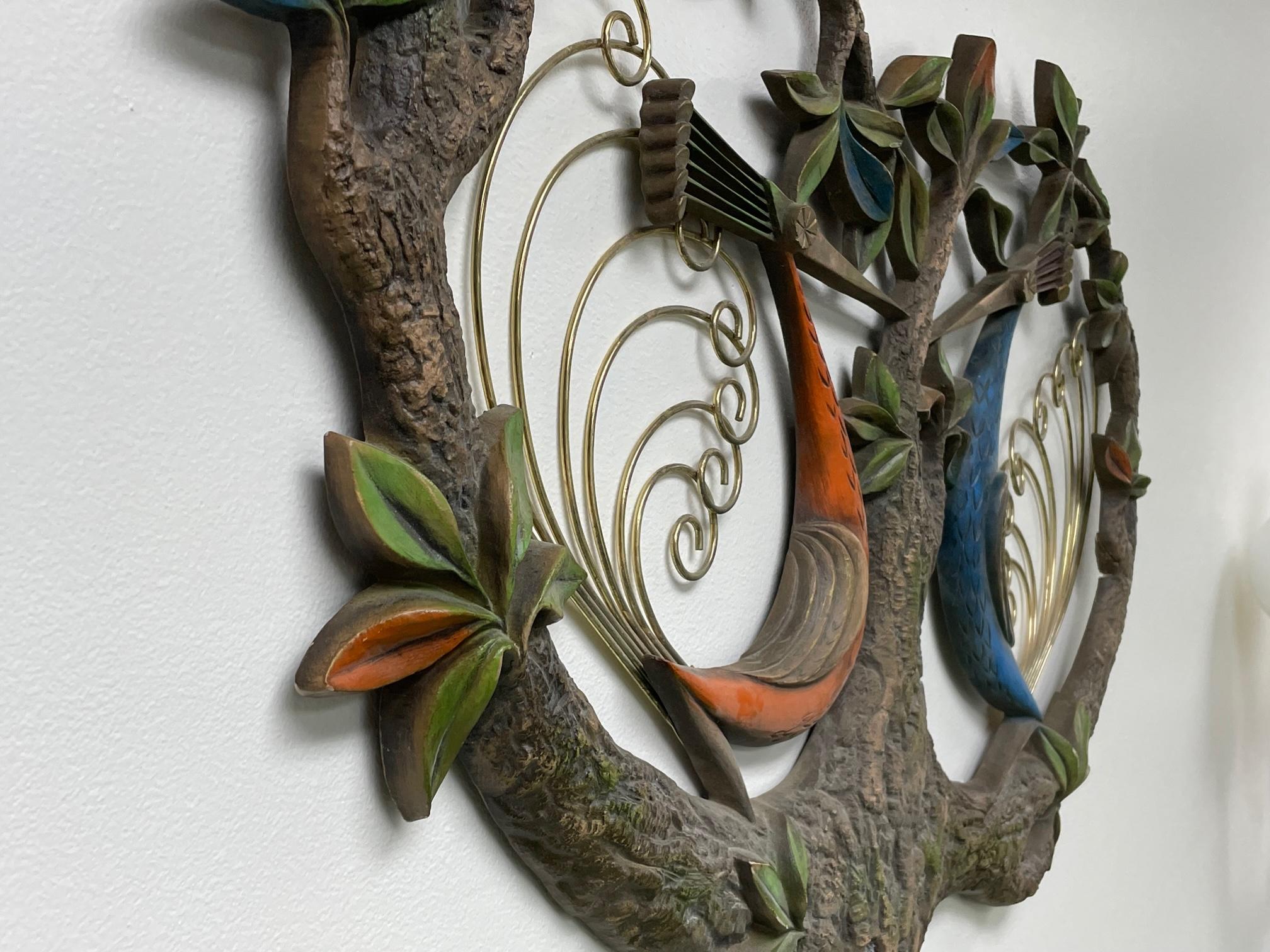 Modernist tropical or tiki style 3D wall hanging features two peacocks with brass tails perched in a tree. Good condition with minor imperfections. Has had small repairs but hard to notice unless looking at back side. See photos for condition