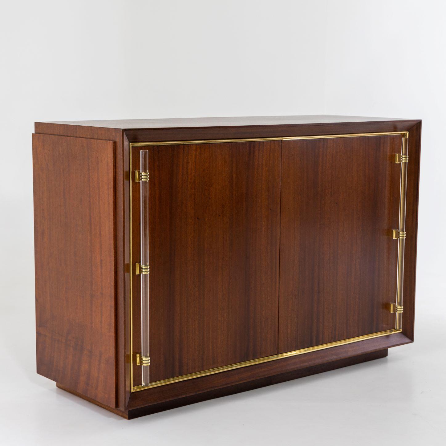 A Modernist two door cabinet. 
Mahogany with glass handles and brass details.
Featuring unique sliding door mechanism.