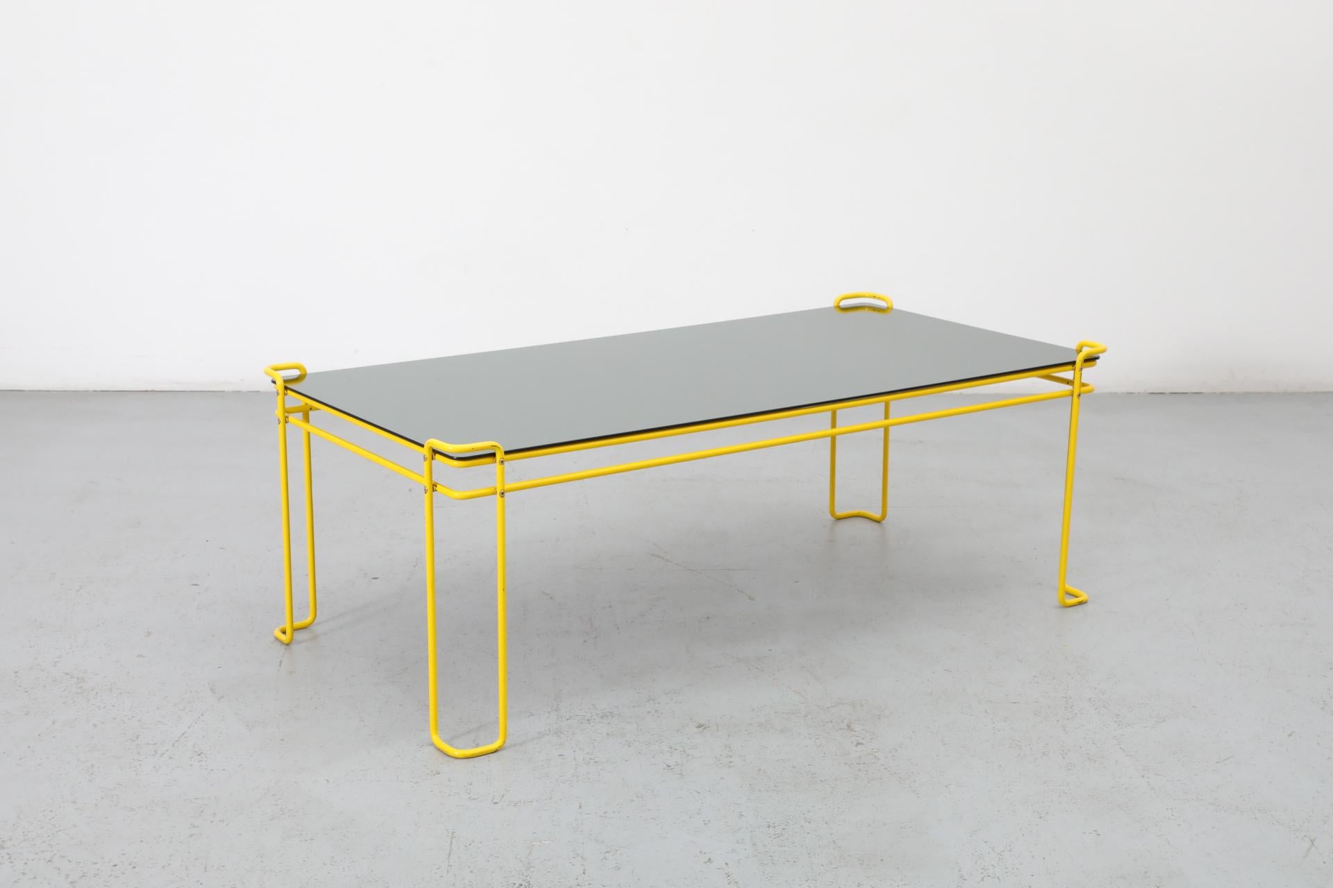 Mesa de centro modernista de alambre esmaltado en amarillo limón con tapa de espejo de cristal ahumado. Fascinante juego sobre el espacio negativo con simples retoques de formas rectangulares de acero tubular doblado que actúan como dispositivos de