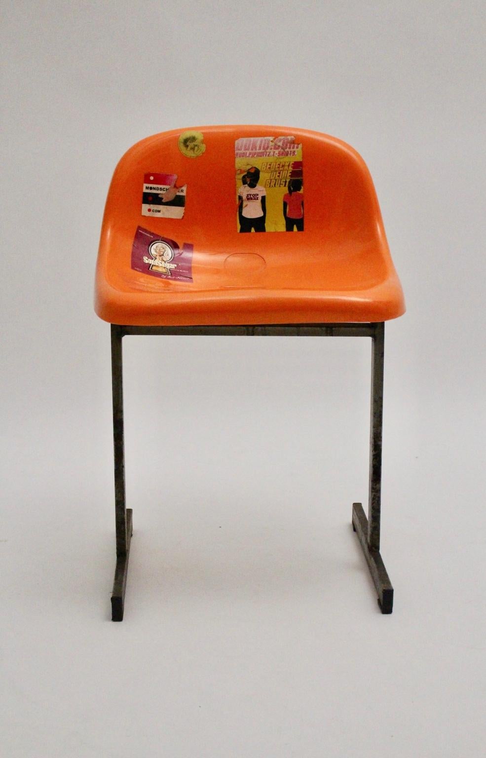 Pop Art vintage plastic metal chair from a sports stadium in Vienna shows a steel frame and an orange plastic seat shell. The seat shell is plastered with many stickers.
Stable and sturdy while the surface of the chair shows signs of use and the