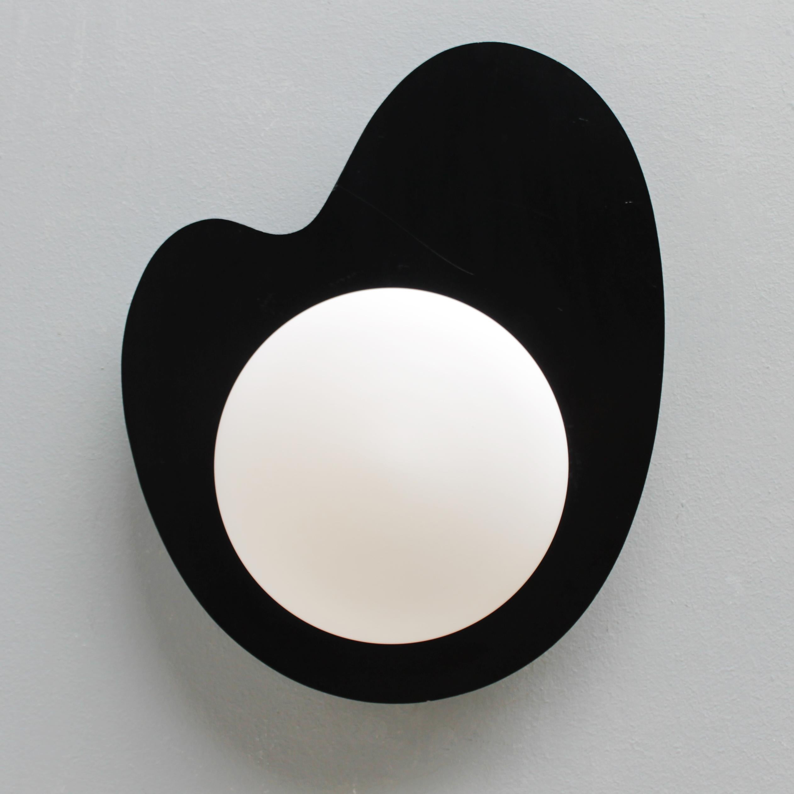 Very rare modernist wall lamp by Kaiser Leuchten, Germany. Period 1950-1960. 
Opaline glass hemisphere on an amorphous black plywood background. Marked with a label.
Dimensions: Height 17.3 in. (44 cm), depth 5.9 in. (10 cm) and width 13.8 inches