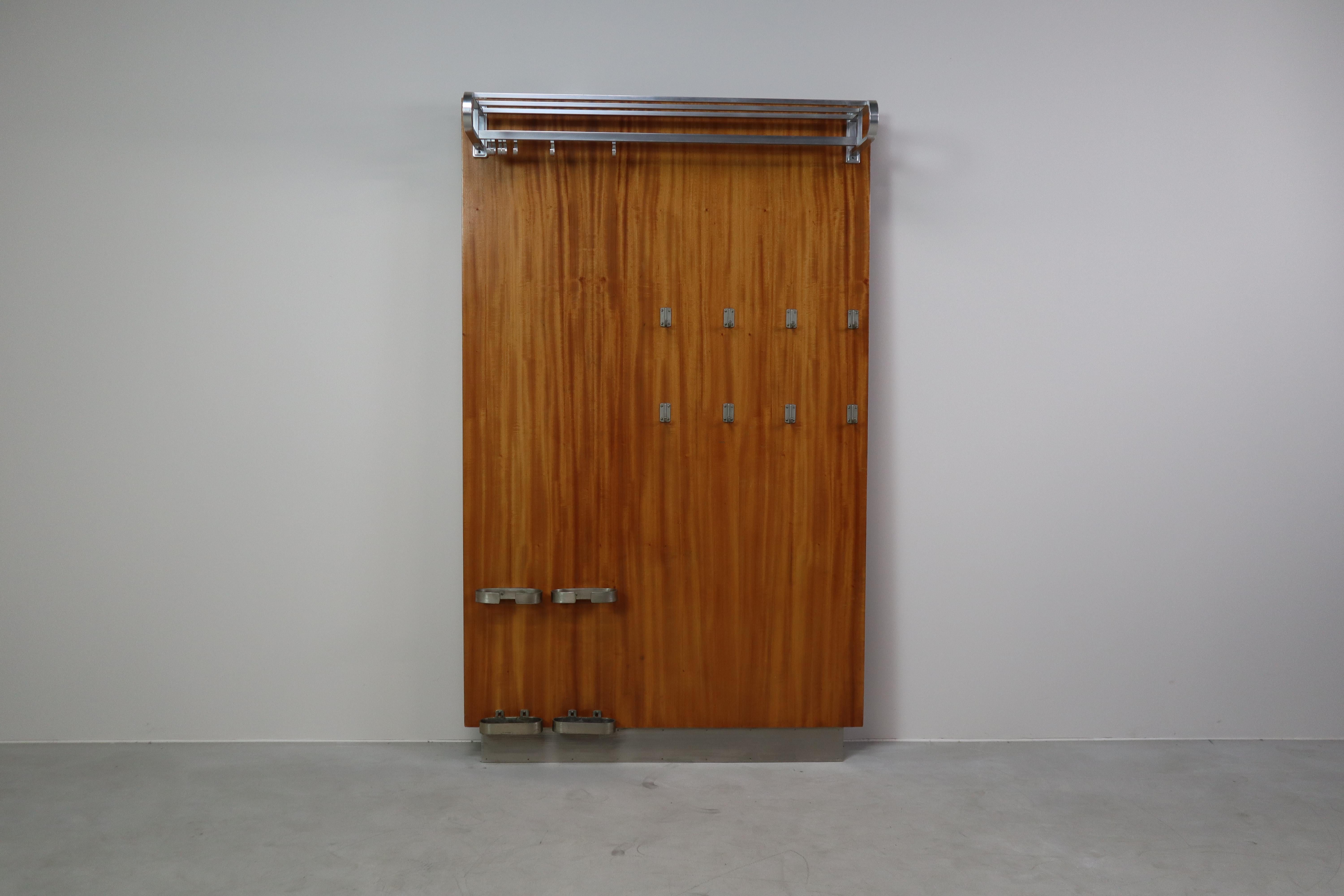 A striking mid-century modernist wall-mounted cloakroom panel in warm Teak veneer, fitted with elegant metal details.
The top features a streamlined Aluminium hat and luggage rack with rounded ends, complete with hanging hooks underneath. The