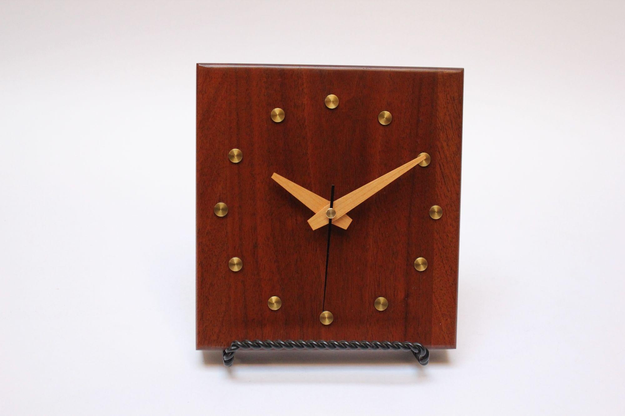 Reloj de pared cuadrado moderno de mediados de siglo en madera de nogal con agujas horaria y minutera de pino (ca. 1970s, EEUU).
Forma sencilla y modernista realzada por adornos redondos de latón que representan los indicadores de las horas.