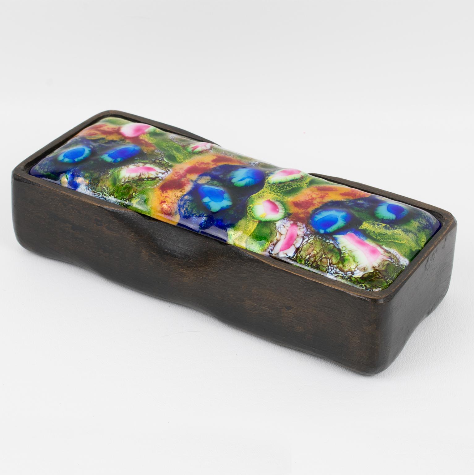 J. Capo Esmaltes diseñó esta hermosa caja con tapa decorativa de mediados de siglo. La pieza se fabricó en España hacia 1960. La forma rectangular ostenta una base contenedora de madera tallada con un encantador toque orgánico. La tapa de esmalte
