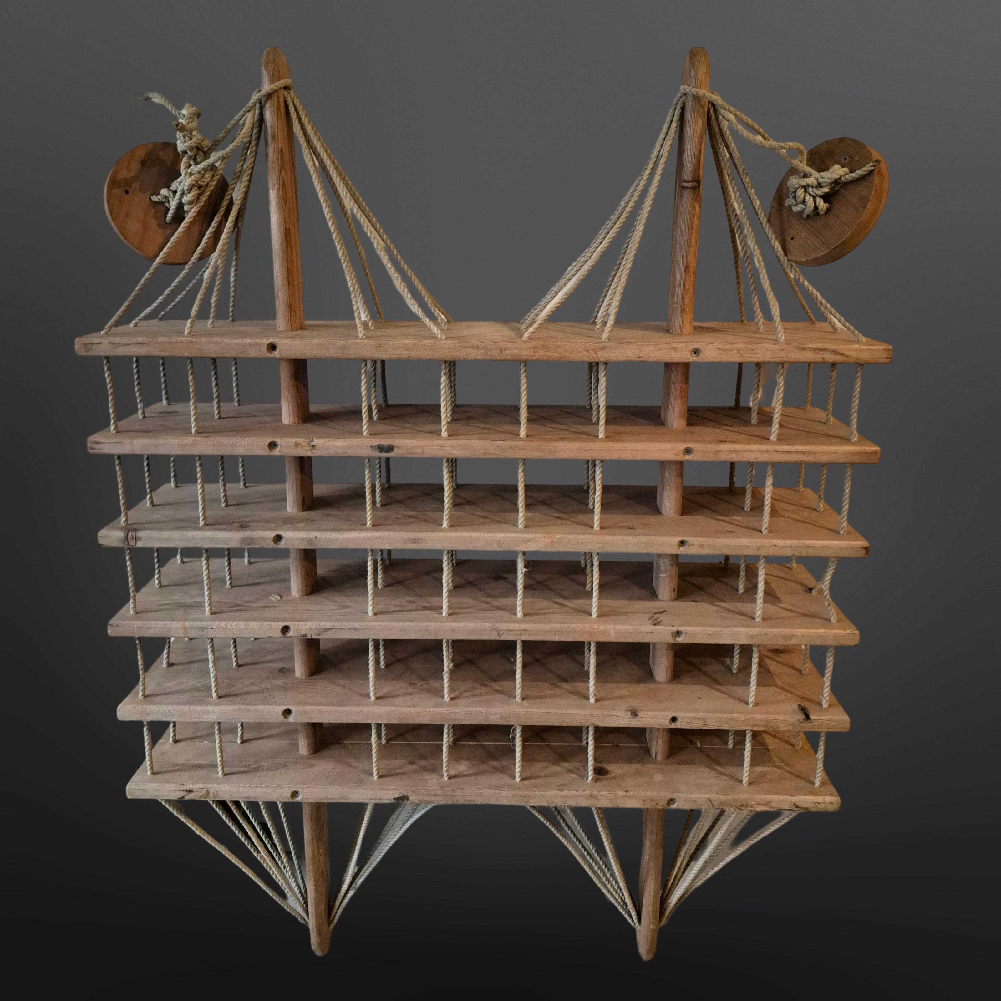 Modernistisches hängendes Weinregal. Handgefertigt aus Massivholz und Seil.
Dieses in den 1970er Jahren in den Niederlanden hergestellte Einzelstück wird mit zwei hölzernen Deckenplatten an der Decke aufgehängt. Er kann bis zu 45 Flaschen