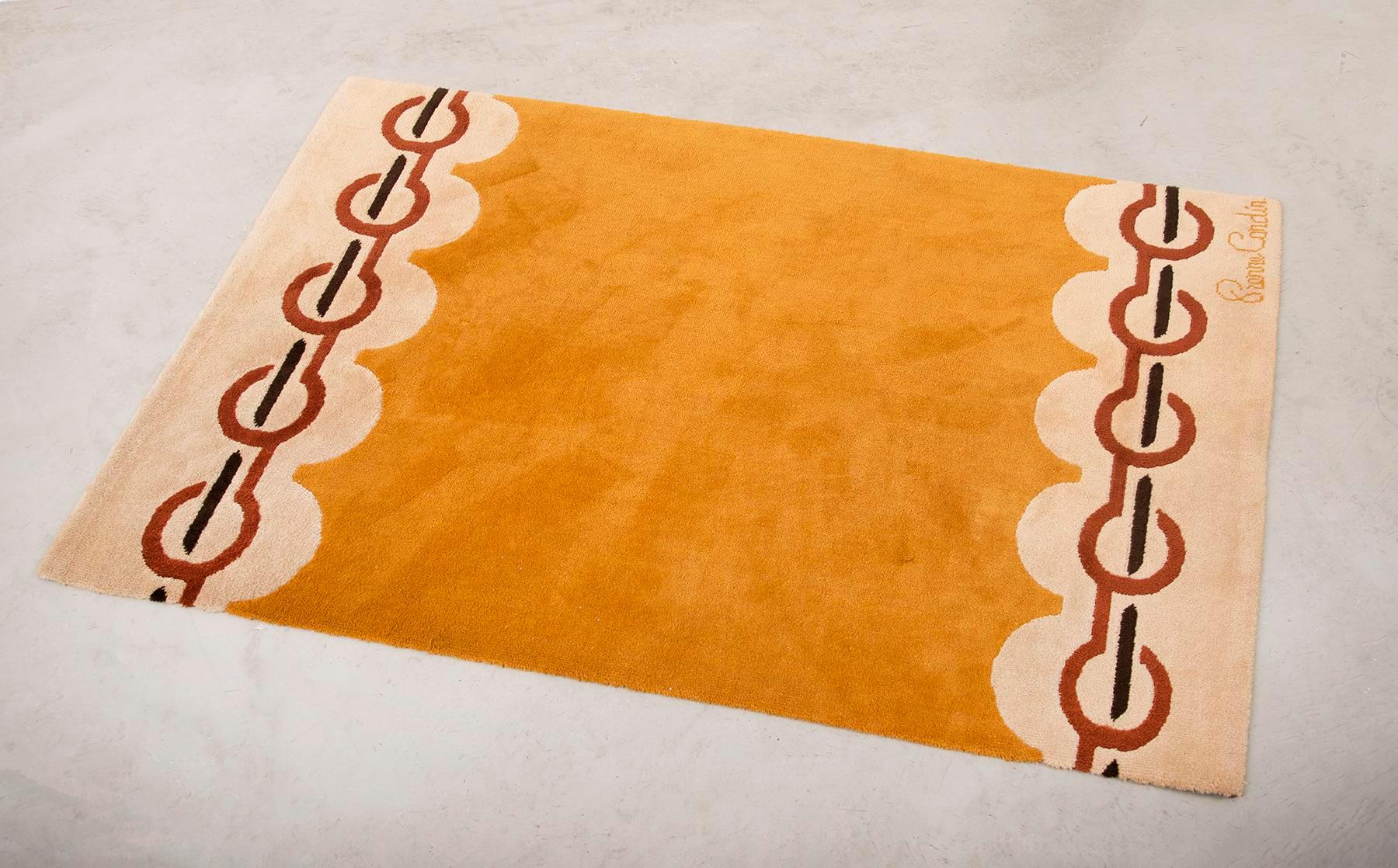 Elegant vintage wool rug designed in Pierre Cardin's Paris Atelier and made in Denmark by Scandinavian Folklore Carpets, 1970s. Vibrant colors in golden yellow, cream, burnt red and coffee brown. Signature in corner.