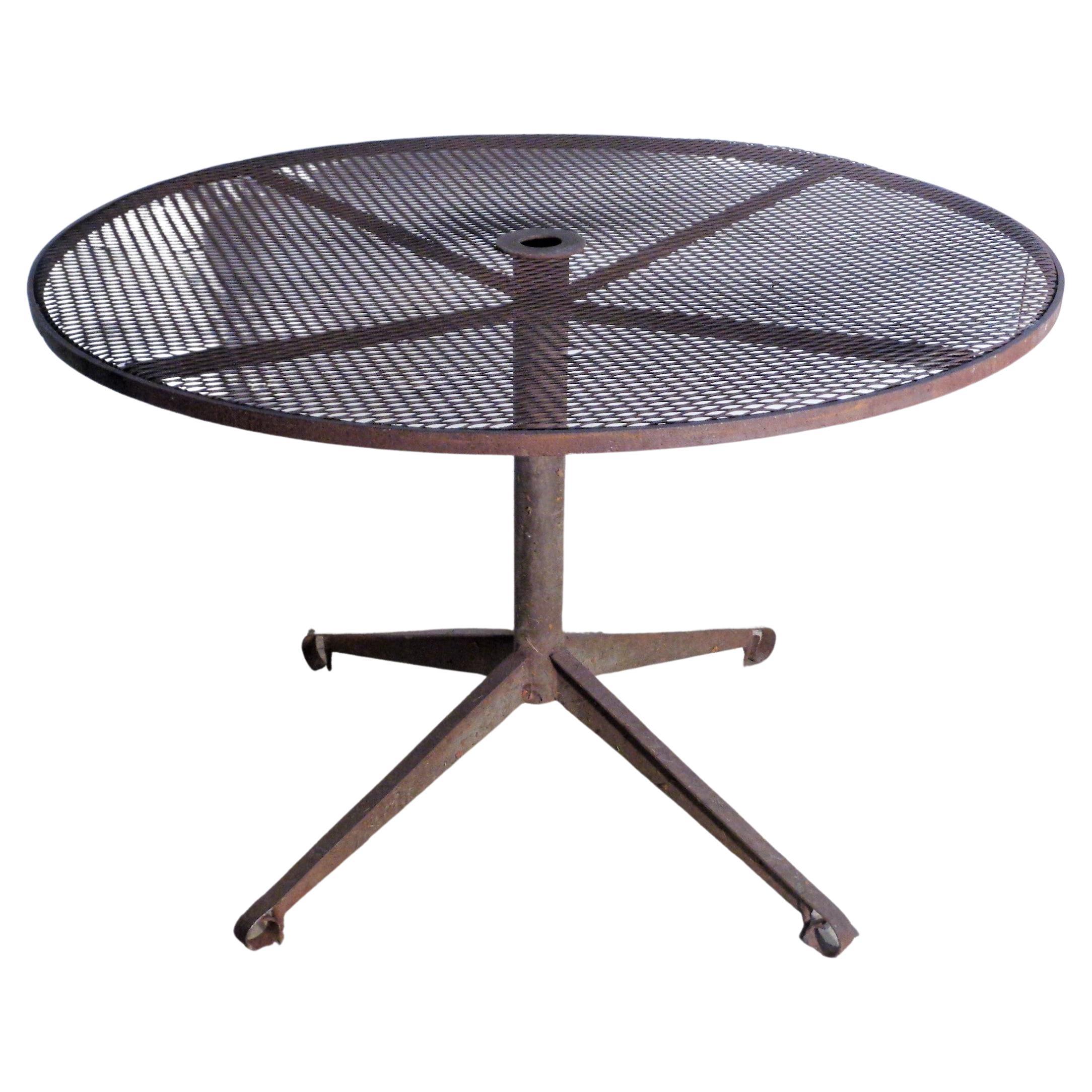  Modernist wrought iron dining table for garden patio. Round steel mesh top w/ hole for umbrella / pedestal base ending in four beautifully angled legs. Attributed to Russell Woodard Sculptura. Circa 1950's. Measures 41