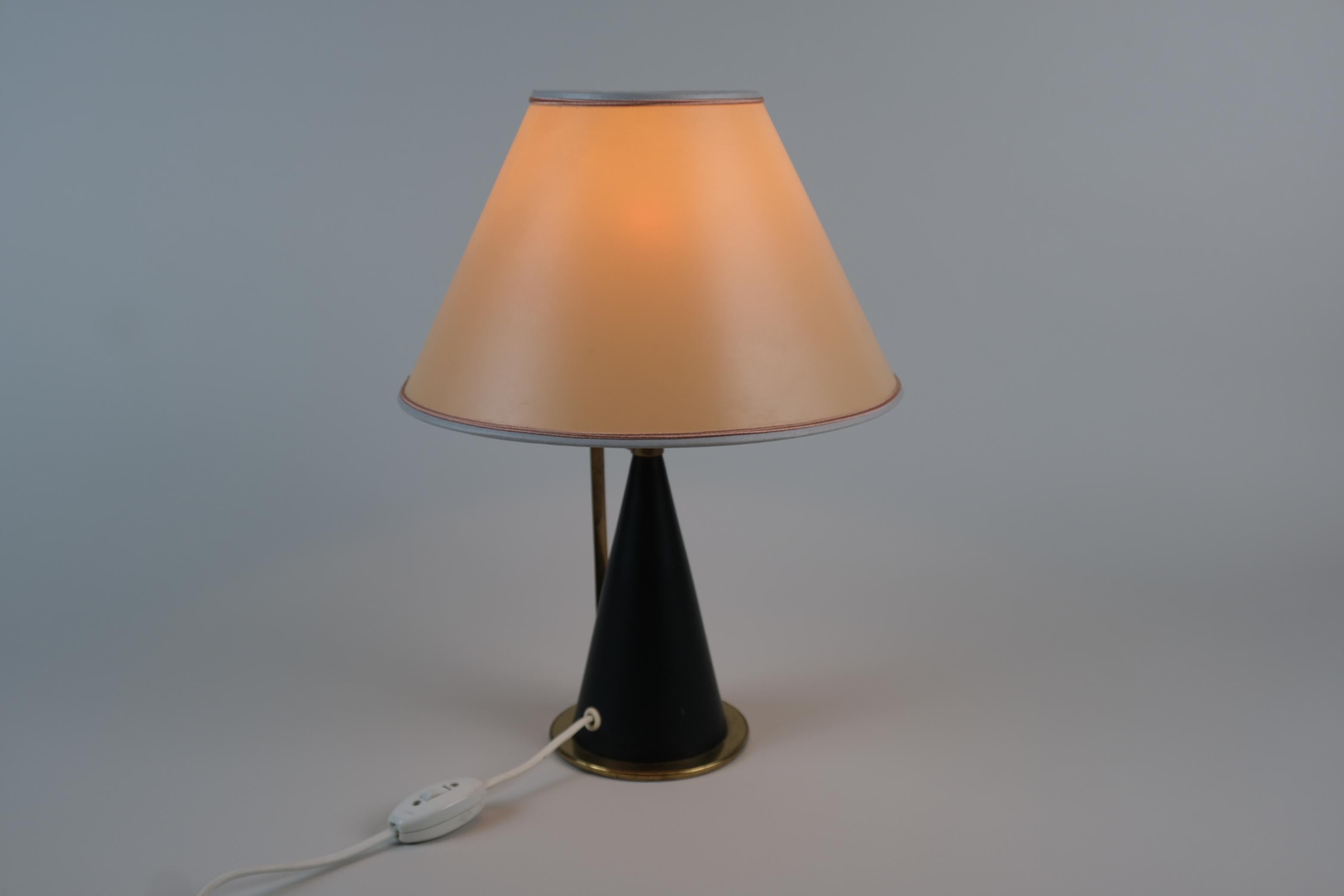 A Mid-Century Modern table lamp model K11-24 by Maria Lindeman for Idman from the 1950s. This rare lamp features a black cone-shaped body with brass details and handle. The original shade with the Stockmann label is made of parchment or