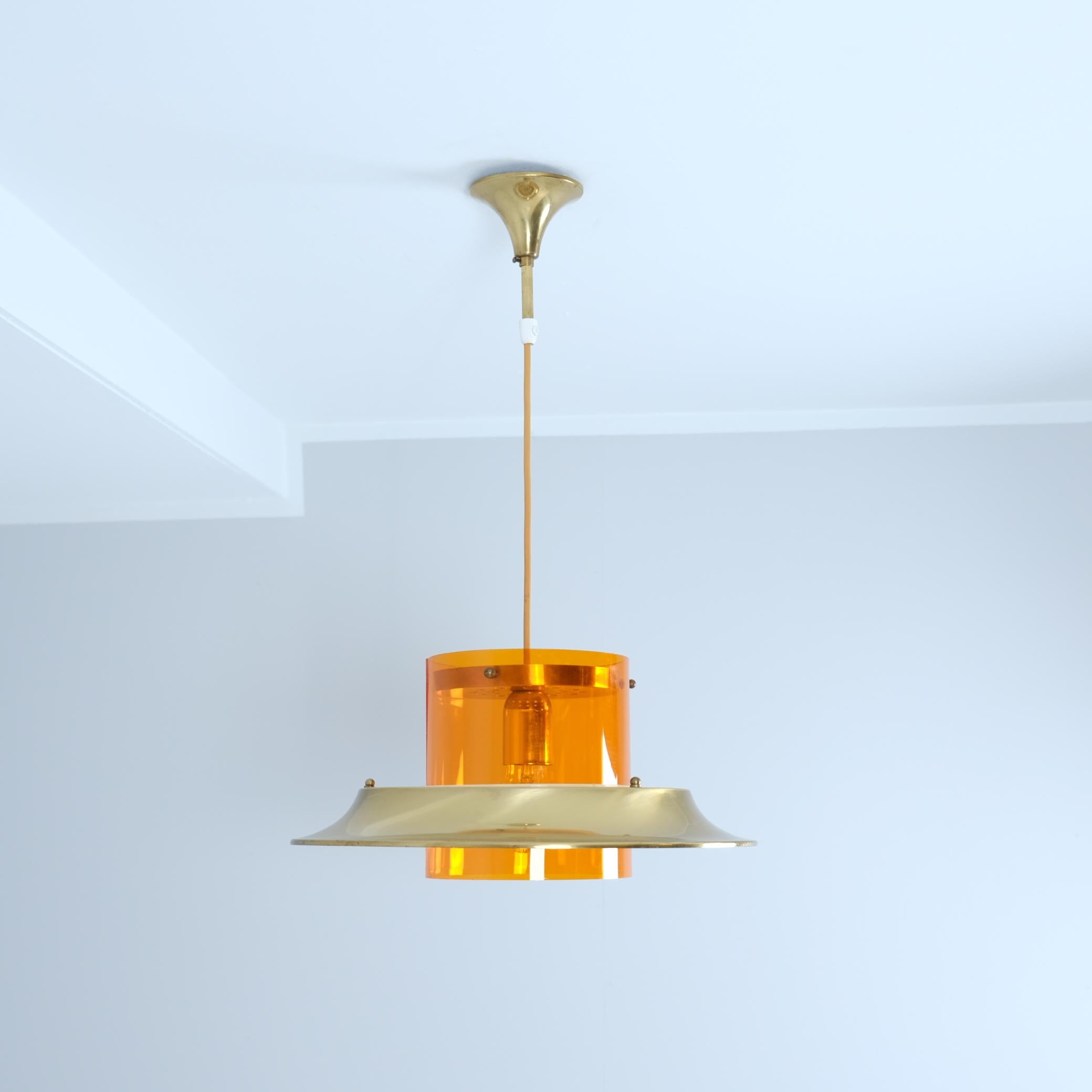 Una sospensione da soffitto straordinariamente modernista realizzata dal designer finlandese Kai Ruokonen (Finnmark), caratterizzata da vistose lamelle in ottone e da un diffusore di luce in acrilico di colore arancione. Questo pezzo futuristico