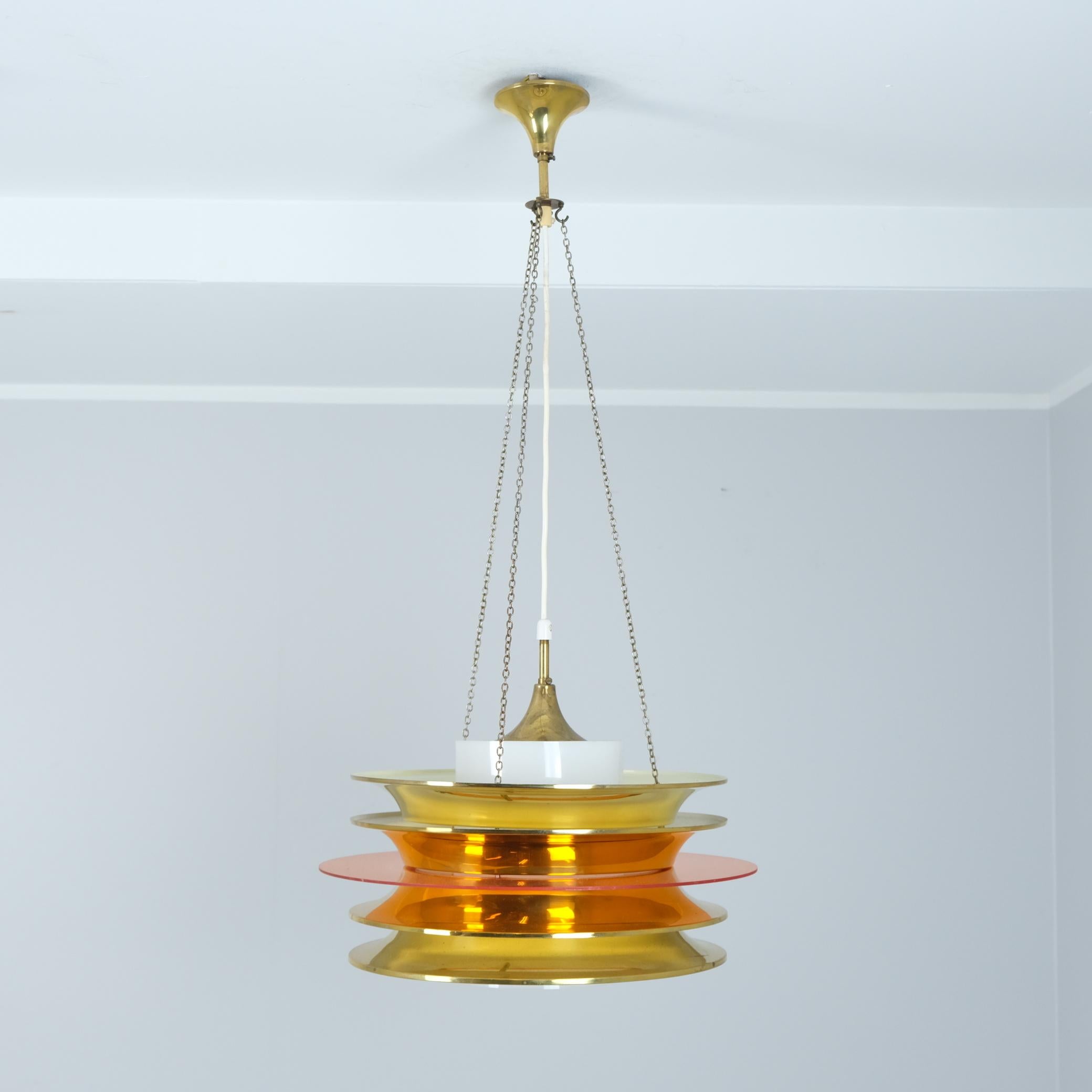 Una sospensione da soffitto a doghe modernista del designer finlandese Kai Kai (Finnmark) composta da 4 doghe in ottone con un elemento circolare arancione trasparente e un cilindro acrilico bianco come diffusore di luce. Un pezzo futuristico che