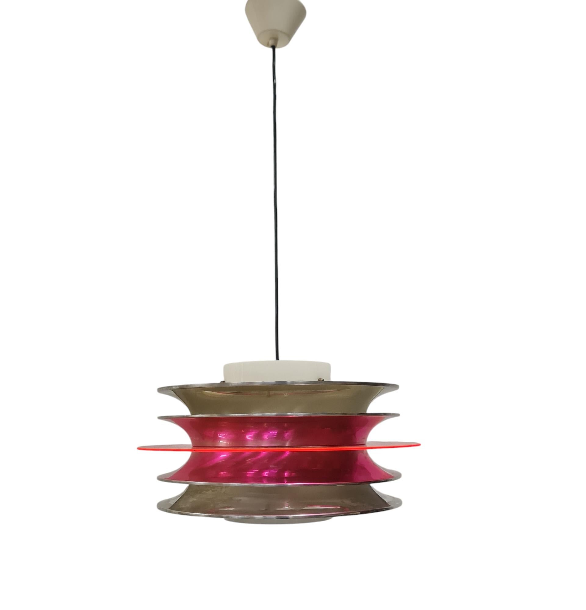 A modernistic slatted ceiling pendant by Finnish designer Kai Ruokonen (Finnmark) consisting of 4 aluminium slates in silver colour with a red see-through circular centerpiece and a white acrylic cylinder as a light diffuser. A futuristic piece that