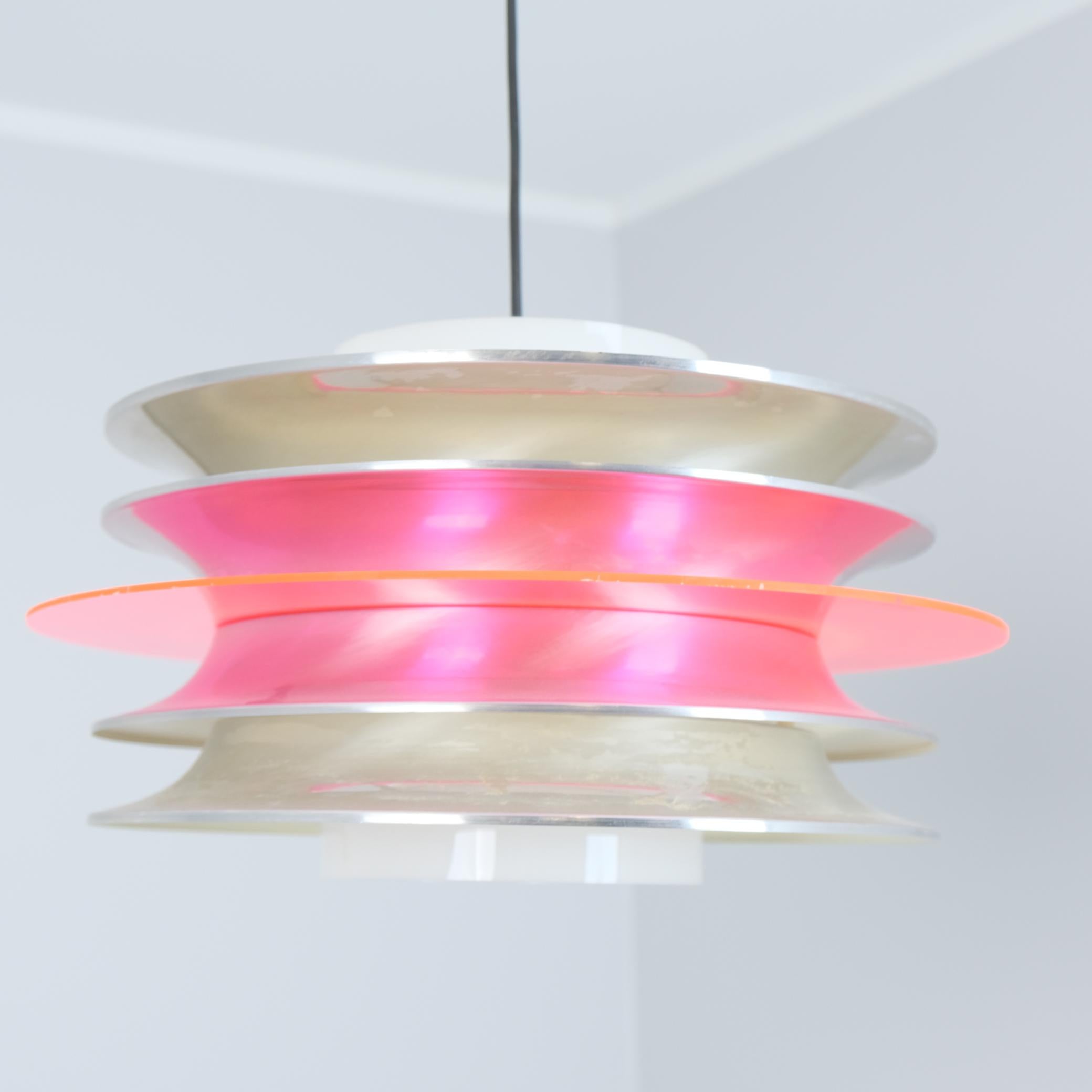 Una sospensione da soffitto a lamelle modernista del designer finlandese Kai Kai (Finnmark) composta da 4 lamelle di alluminio color argento con un elemento circolare rosso trasparente e un cilindro acrilico bianco come diffusore di luce. Un pezzo