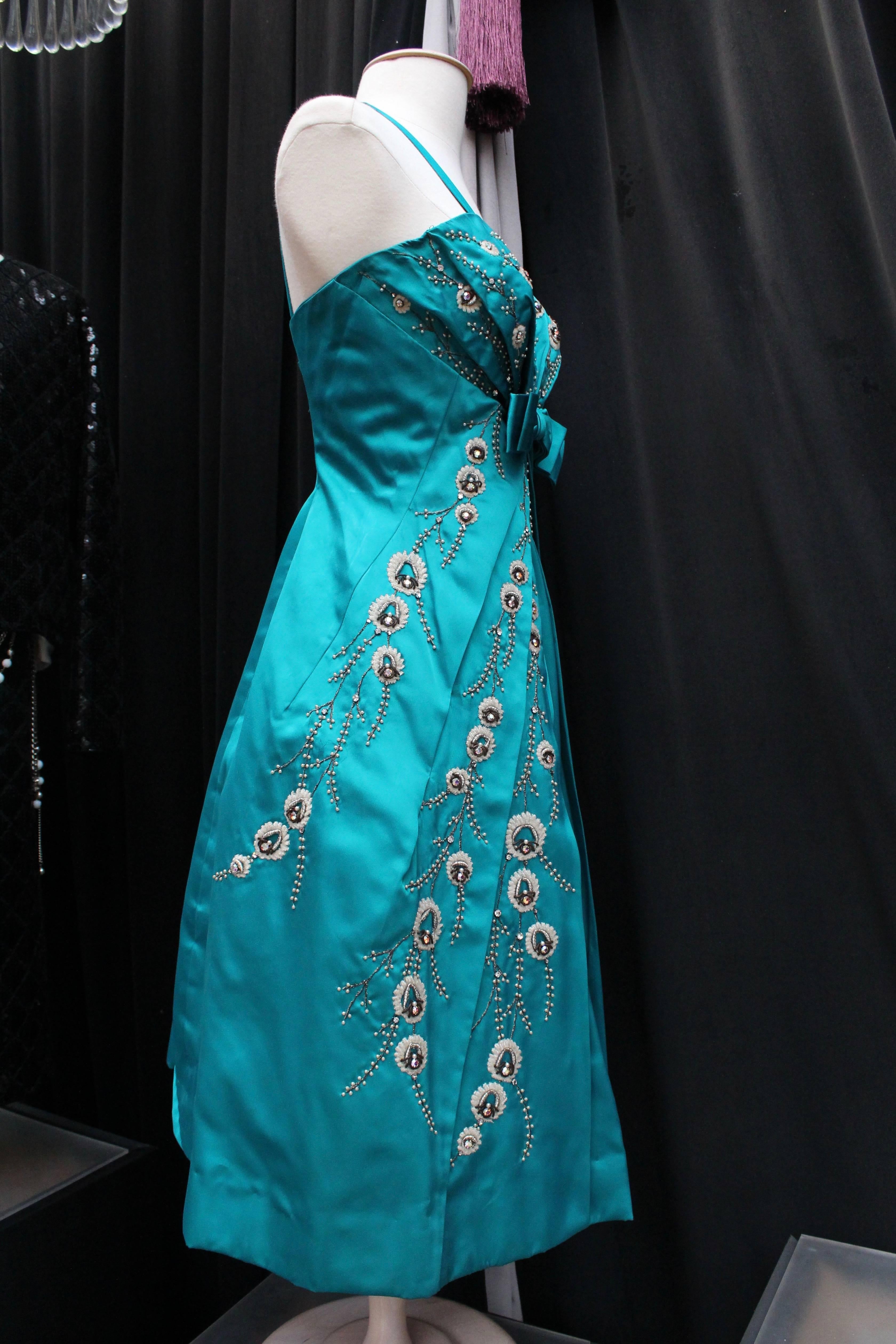 MODISSA – Lovely turquoise satin puffball shaped cocktail dress. It is embellished with a wide bow at bust and pearly beads and rhinestones embroideries representing branches. The delicate pleat work runs upwards from the bow towards the shoulders,
