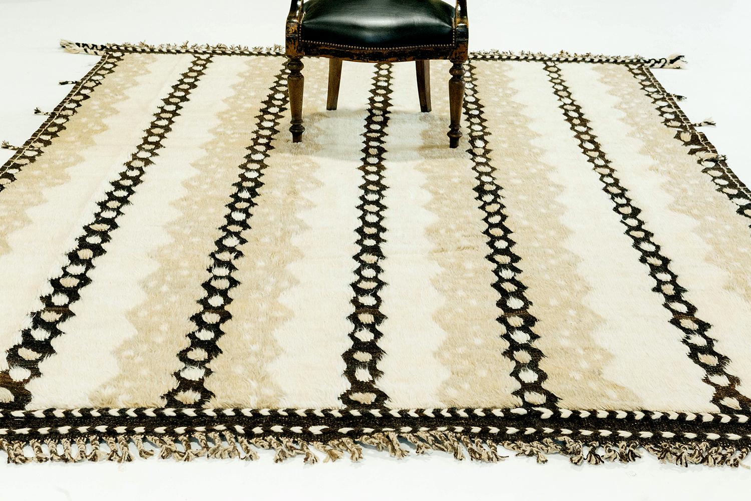 The 'Modlina' rug is a handwoven wool piece inspired by vintage Scandinavian design elements and recreated for the modern design world. The rug's shag balance and harmony, hand woven with a black flat weave and piles of taupe and ivory. This