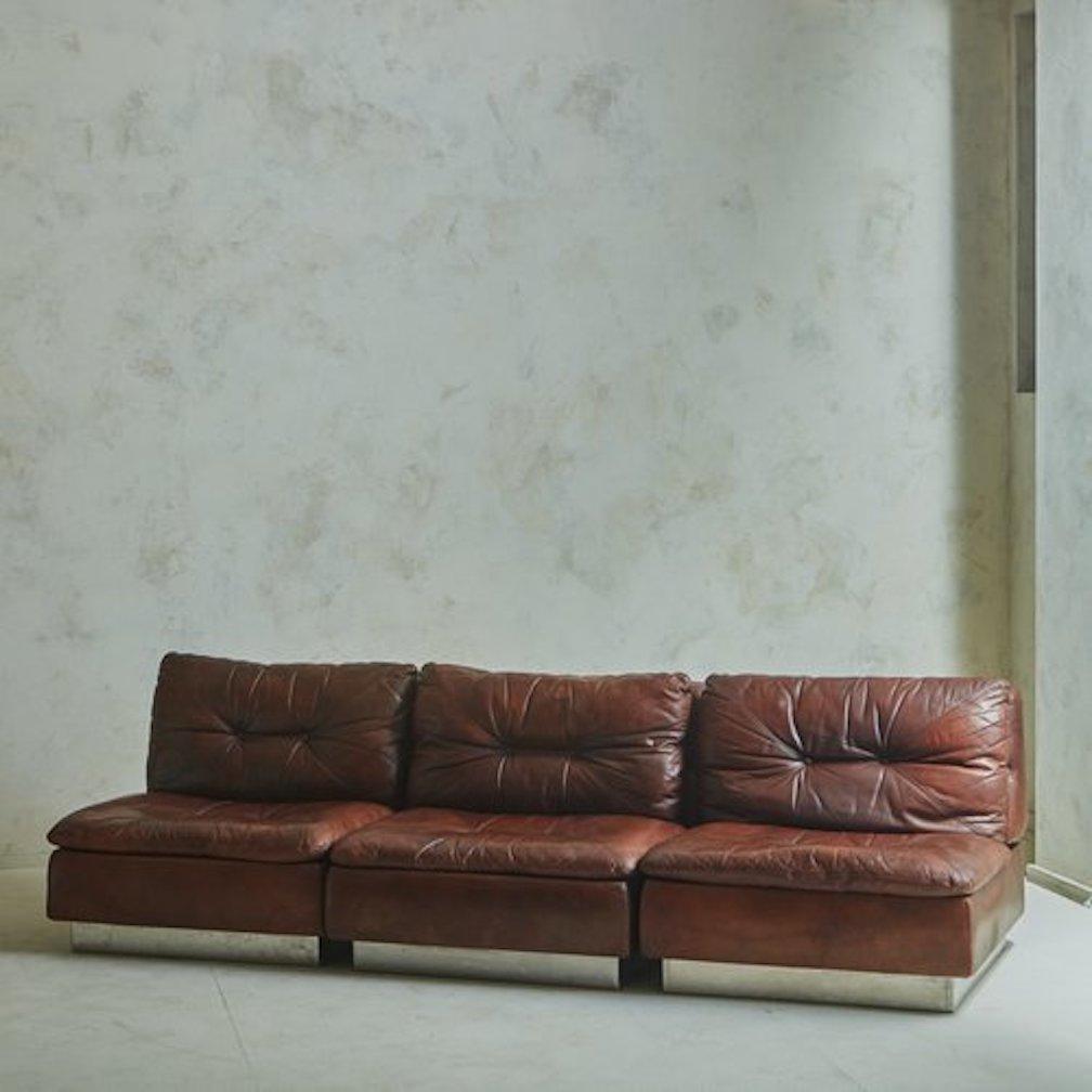 A 1970s Italian three-piece sofa by Saporiti in original patinated chocolate brown leather with button tufts and stitch detailing. Each section has two removable cushions and stands on a sleek chrome plinth base. The modular design allows this sofa