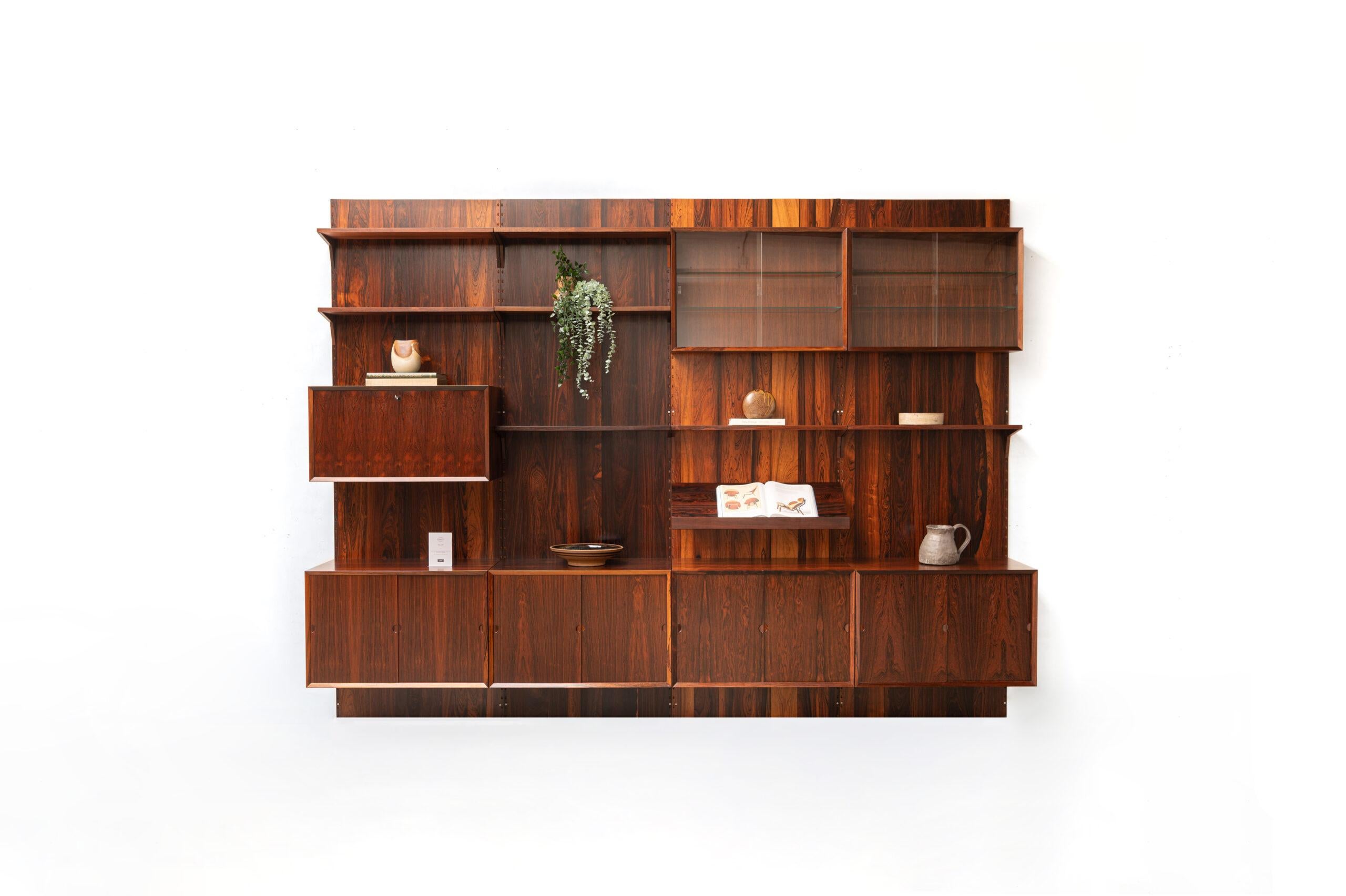 Danish wall unit designed by Poul Cadovius for CADO, Denmark. This setup is in rosewood and has four storage cabinets, one bar cabinet, two display cabinets, one display shelf and seven shelves. Always adaptable and further