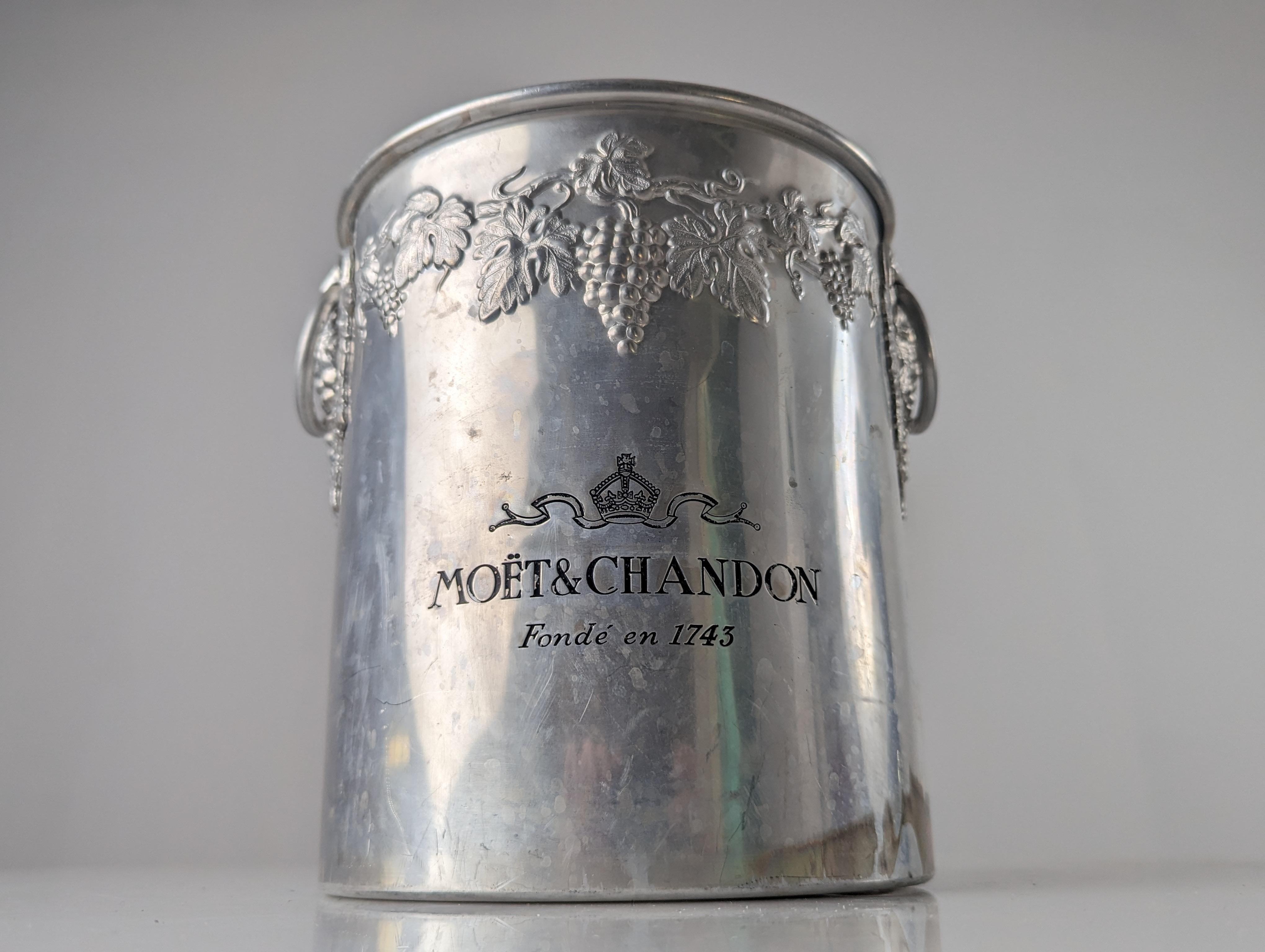 Elegant champagne bucket from the exclusive brand MOET & CHANDON with a beautiful floral decoration of a vine with bunches of grapes surrounding the top.
