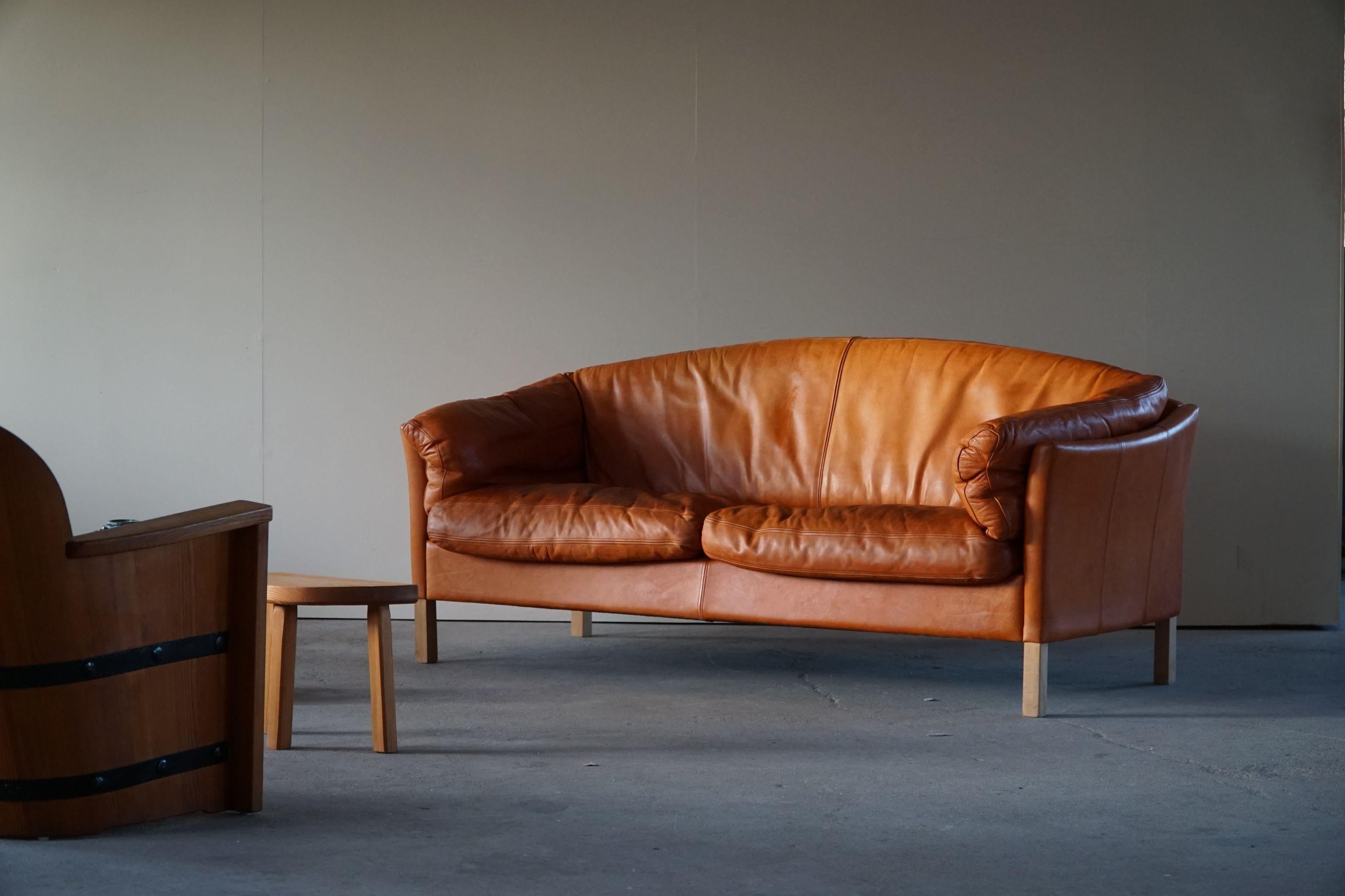 Mid-century Danish 2.5 seater sofa in cognac coloured leather, feets made in beech, Designed by Mogens Hansen for Odense Møbelfabrik in 1970s. Model 535.

Nice curves and a stunning warm patina in this classic danish sofa.

With a heavy focus on