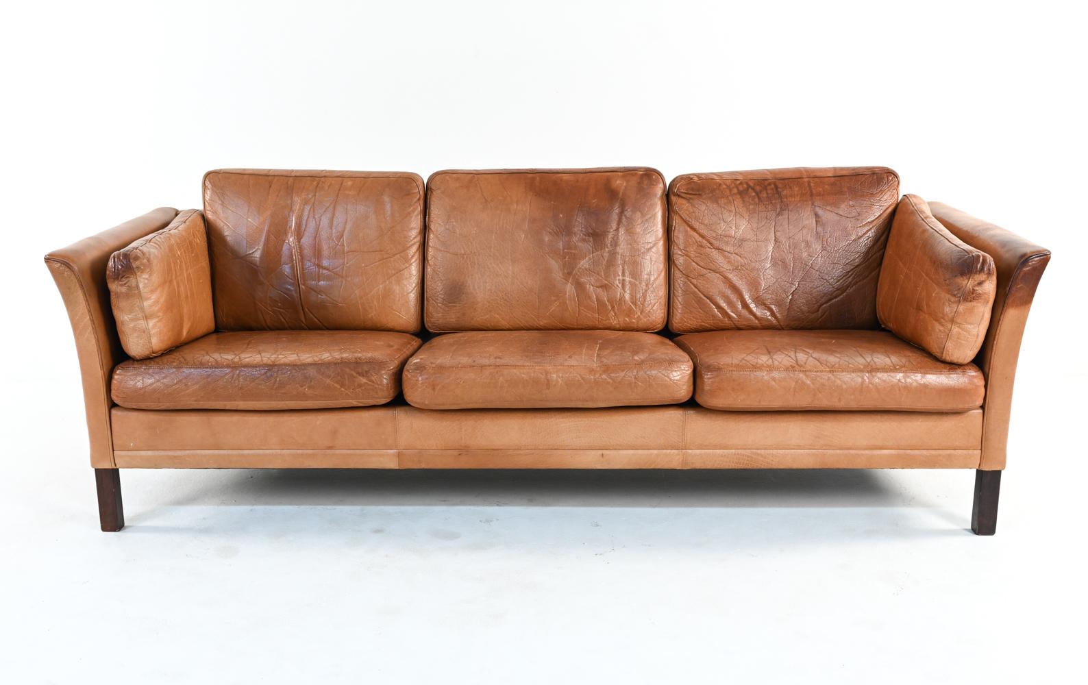 Celebrated for its ideal proportions, fine craftsmanship and ultimate comfort, the Mogens Hansen leather sofa has been a continuous design favorite for over four decades. This three-seater example features dark stained beechwood legs and handsomely