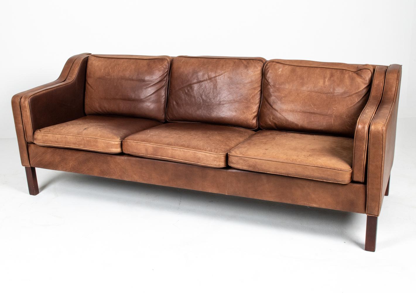 Celebrated for its ideal proportions, fine craftsmanship and ultimate comfort, the Mogens Hansen leather sofa has been a continuous design favorite for over four decades. This example features dark stained beechwood legs and distressed brown leather