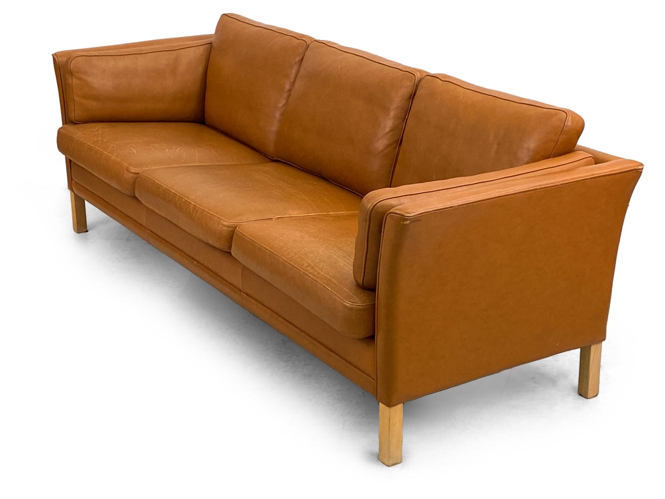Treten Sie ein in ein Reich des luxuriösen Komforts und des unvergleichlichen Designs mit dem Mogens Hansen Danish Modern Caramel Leather Three-Seater Sofa. Dieses Sofa, das die Essenz dänischer Handwerkskunst und die schlichte Ästhetik des modernen
